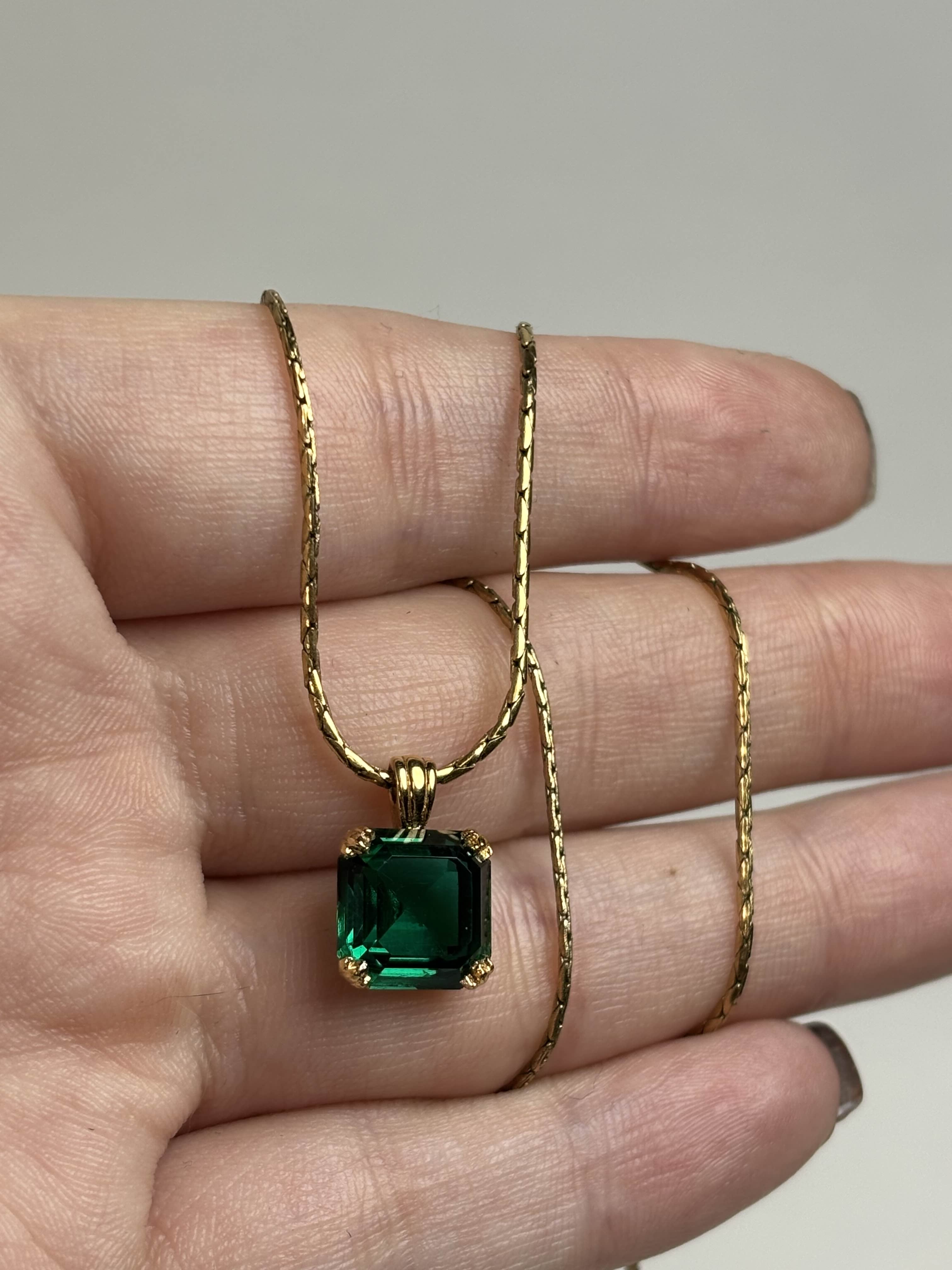 Front of a old necklace with a green gemstone pendant held on a hand against a neutral background