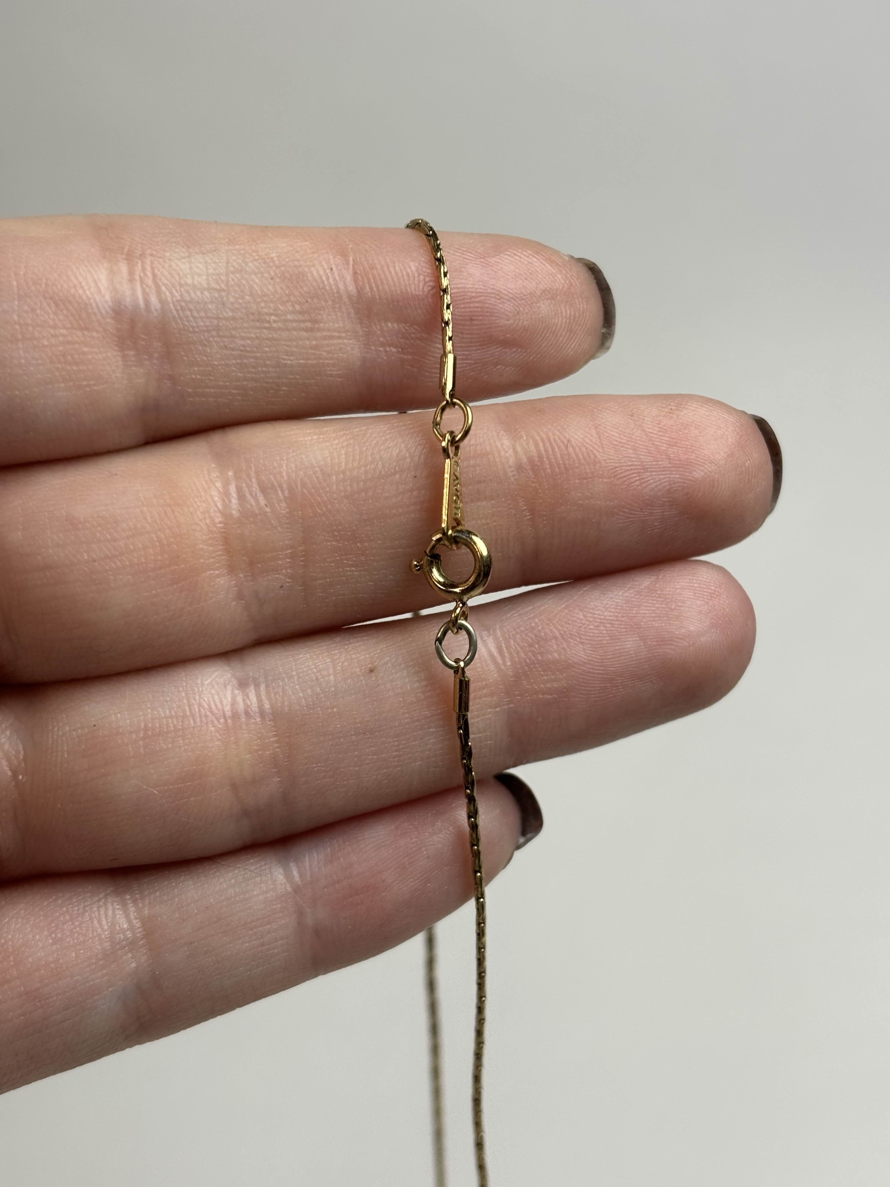 Clasp of a gold necklace being held between fingers against a neutral background