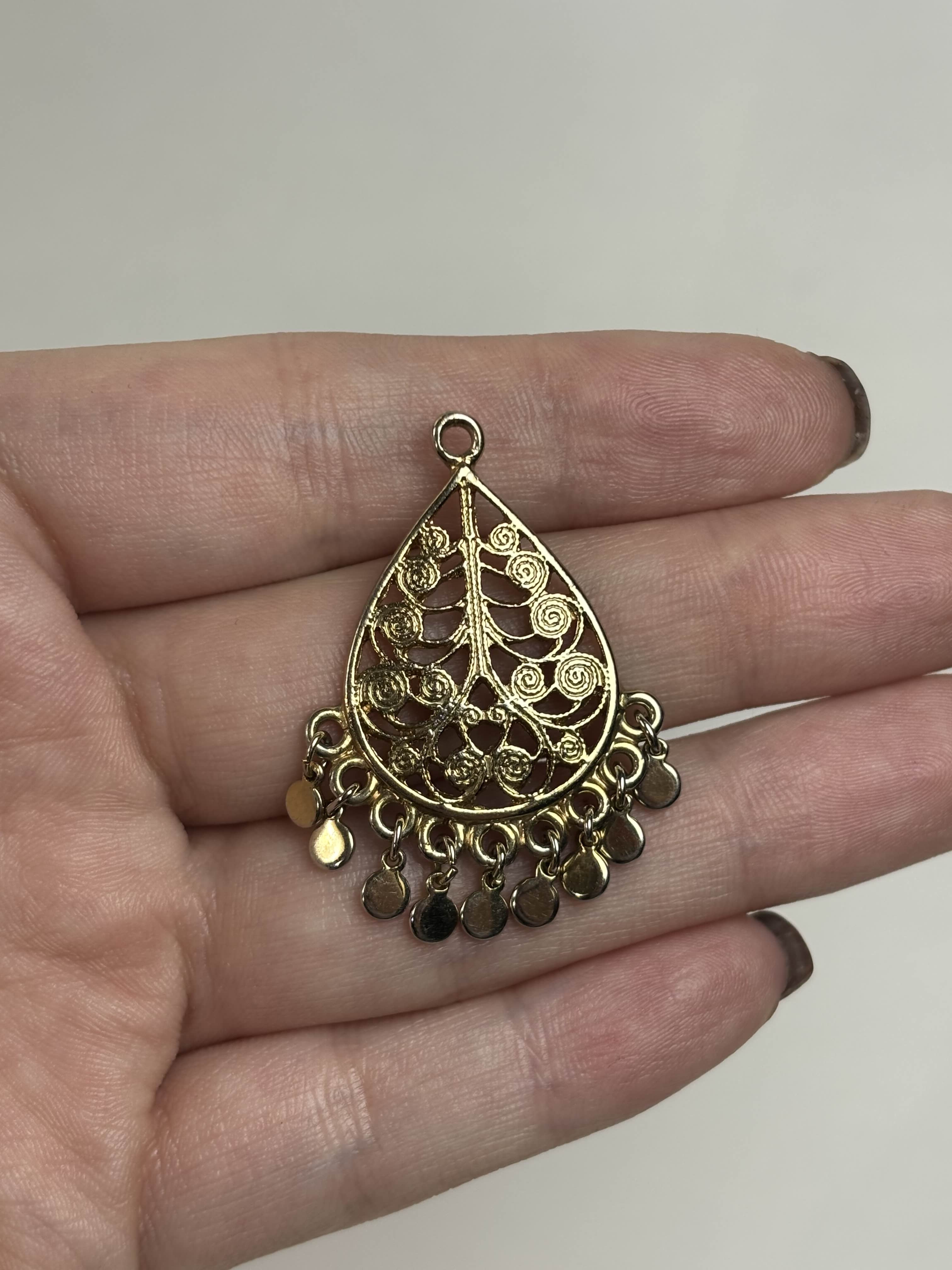 Front of gold teardrop-shaped pendant held in a hand against a neutral background