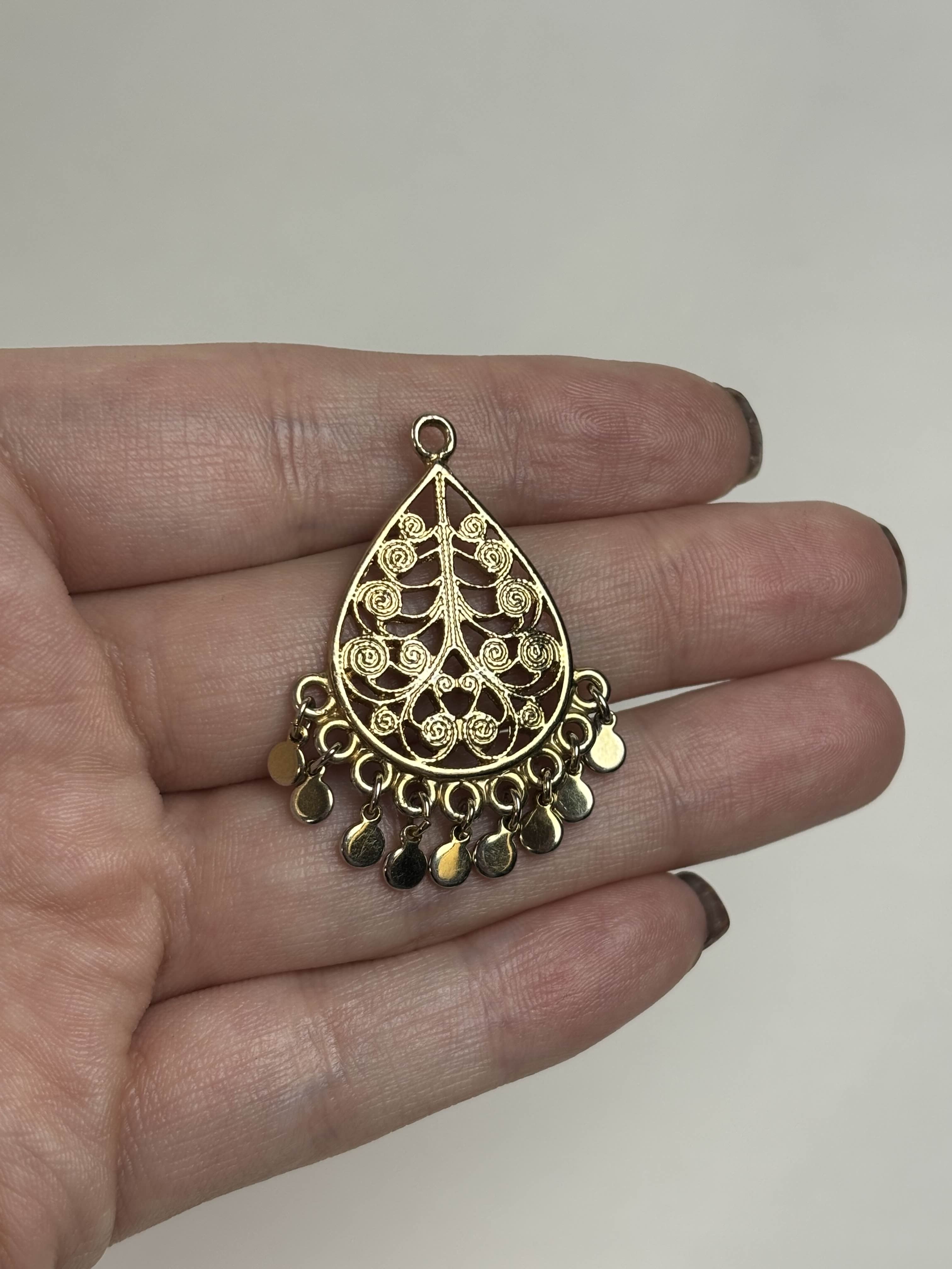 Gold teardrop-shaped pendant held in a hand against a neutral background