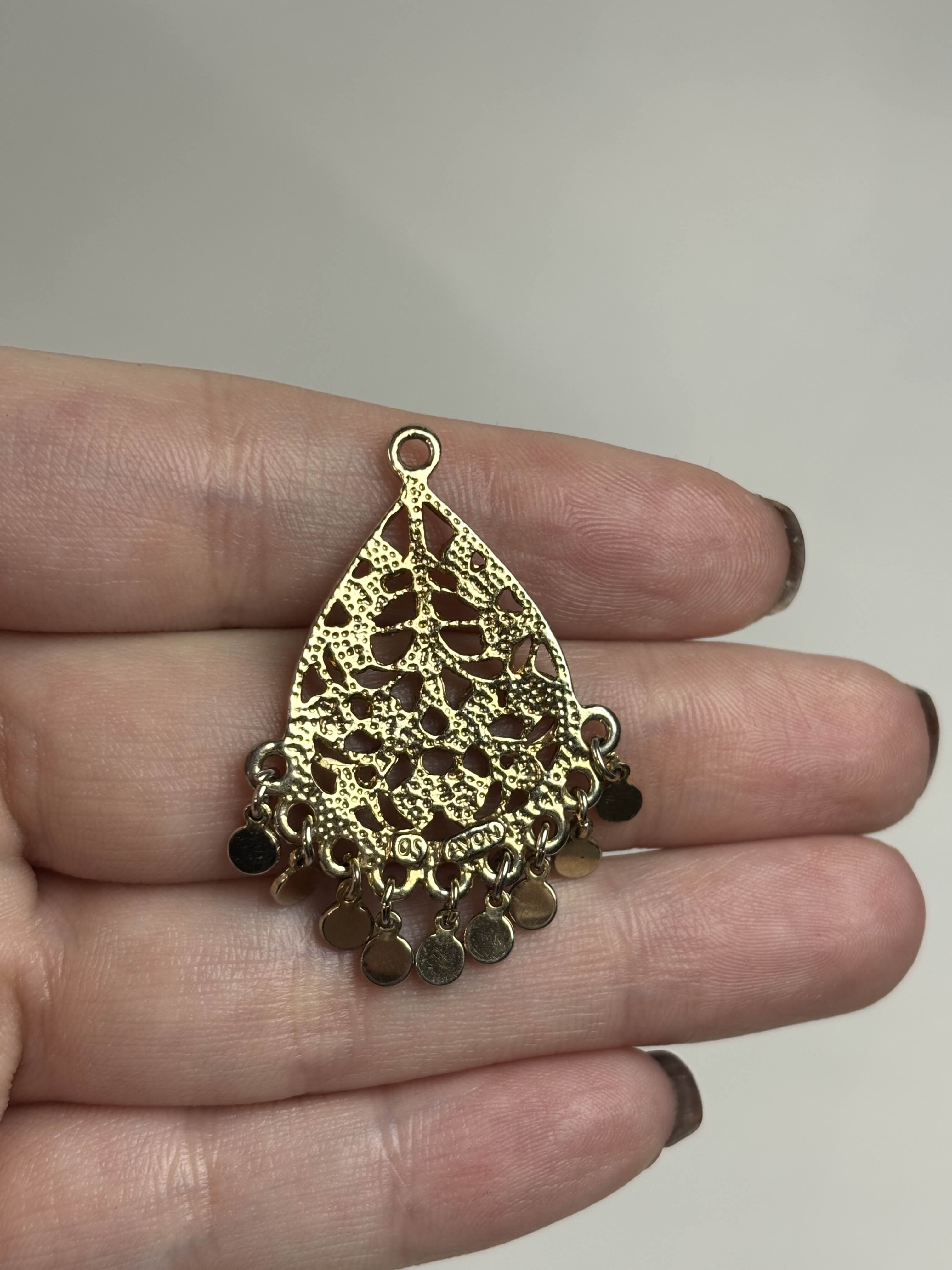 Back of gold teardrop-shaped pendant held in a hand against a neutral background