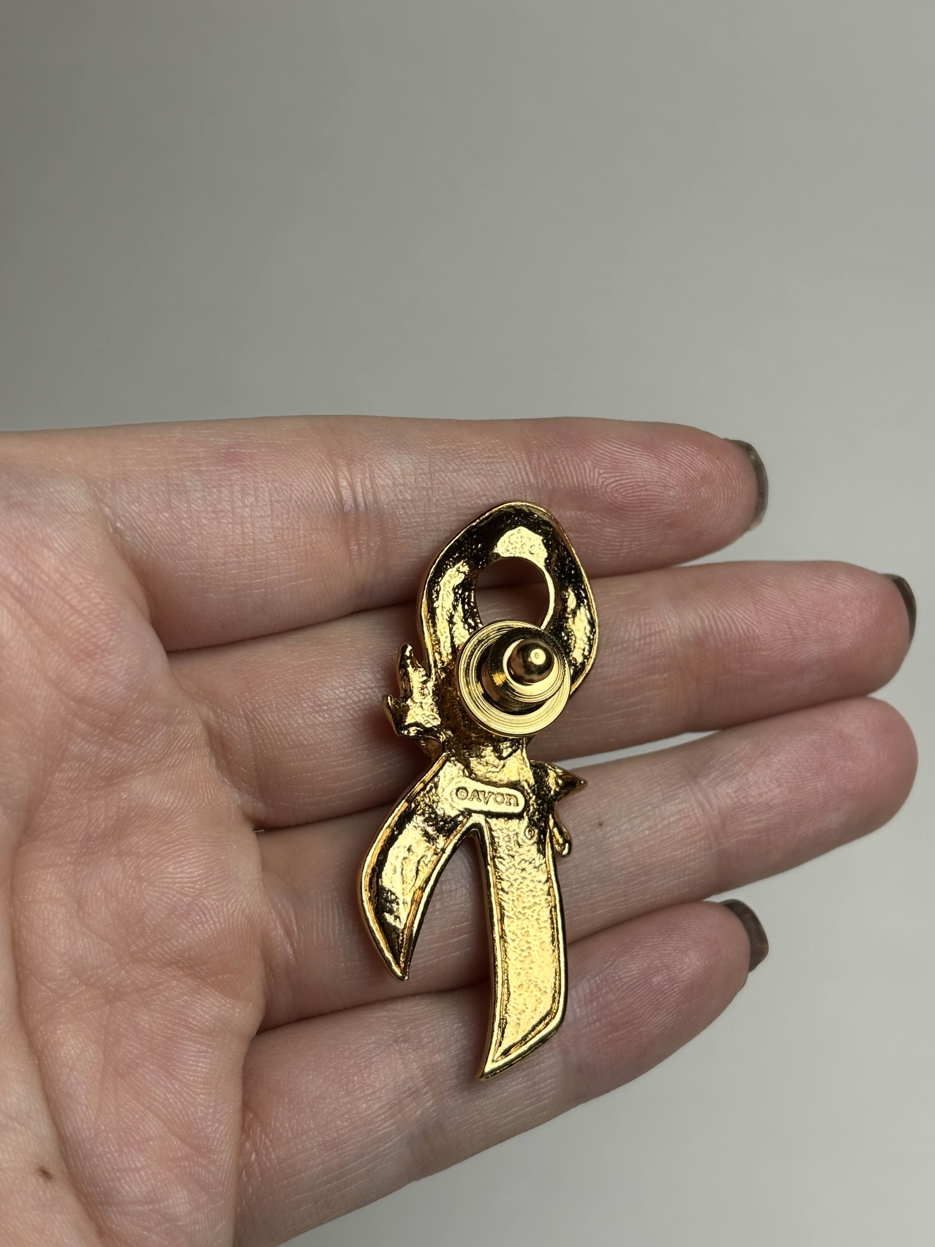 Back of breast cancer awareness ribbon brooch with pink enamel and a gold rose in the center held in a hand against a neutral background