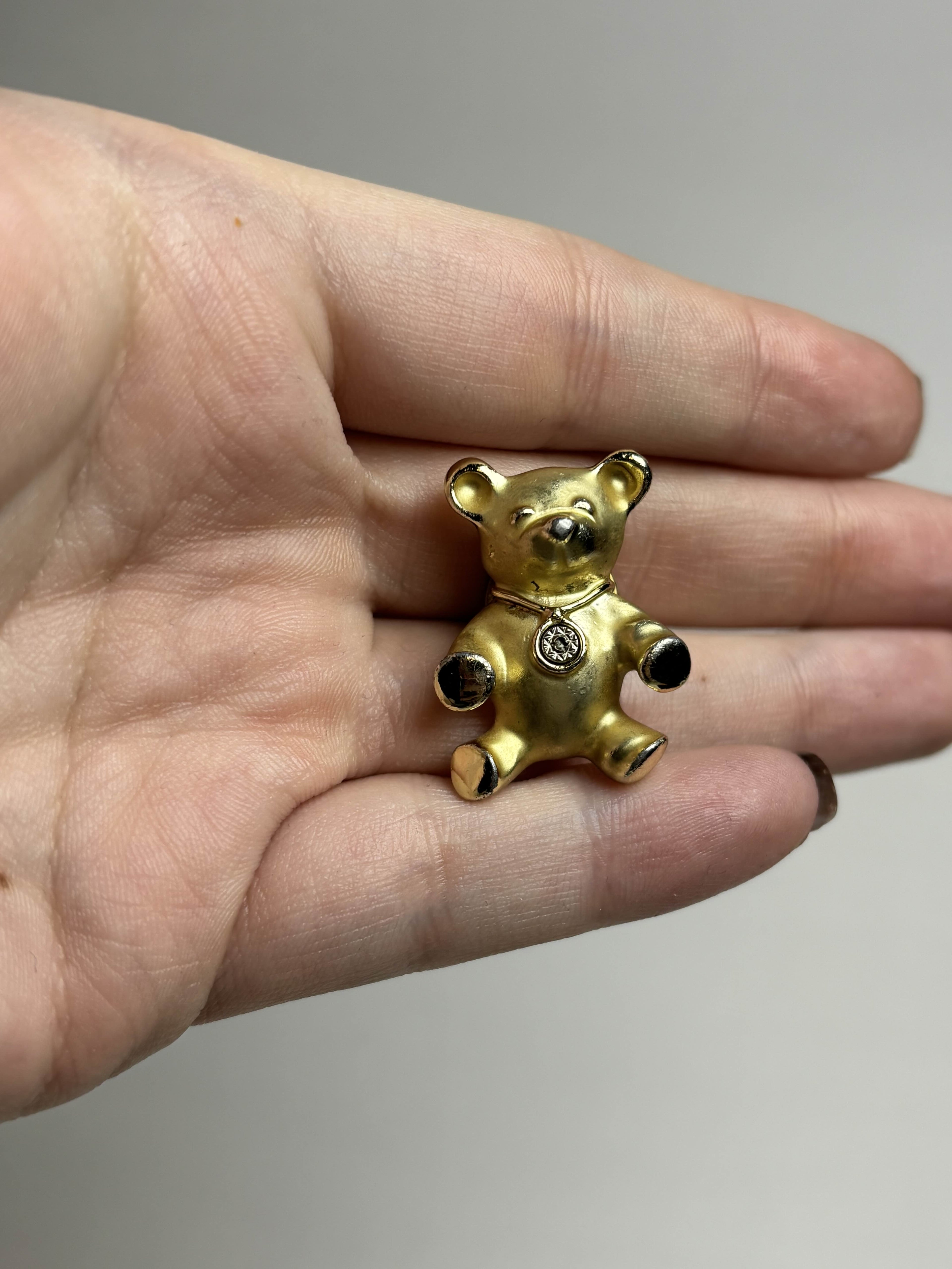 Front of old teddy bear pin held in a hand against a neutral background