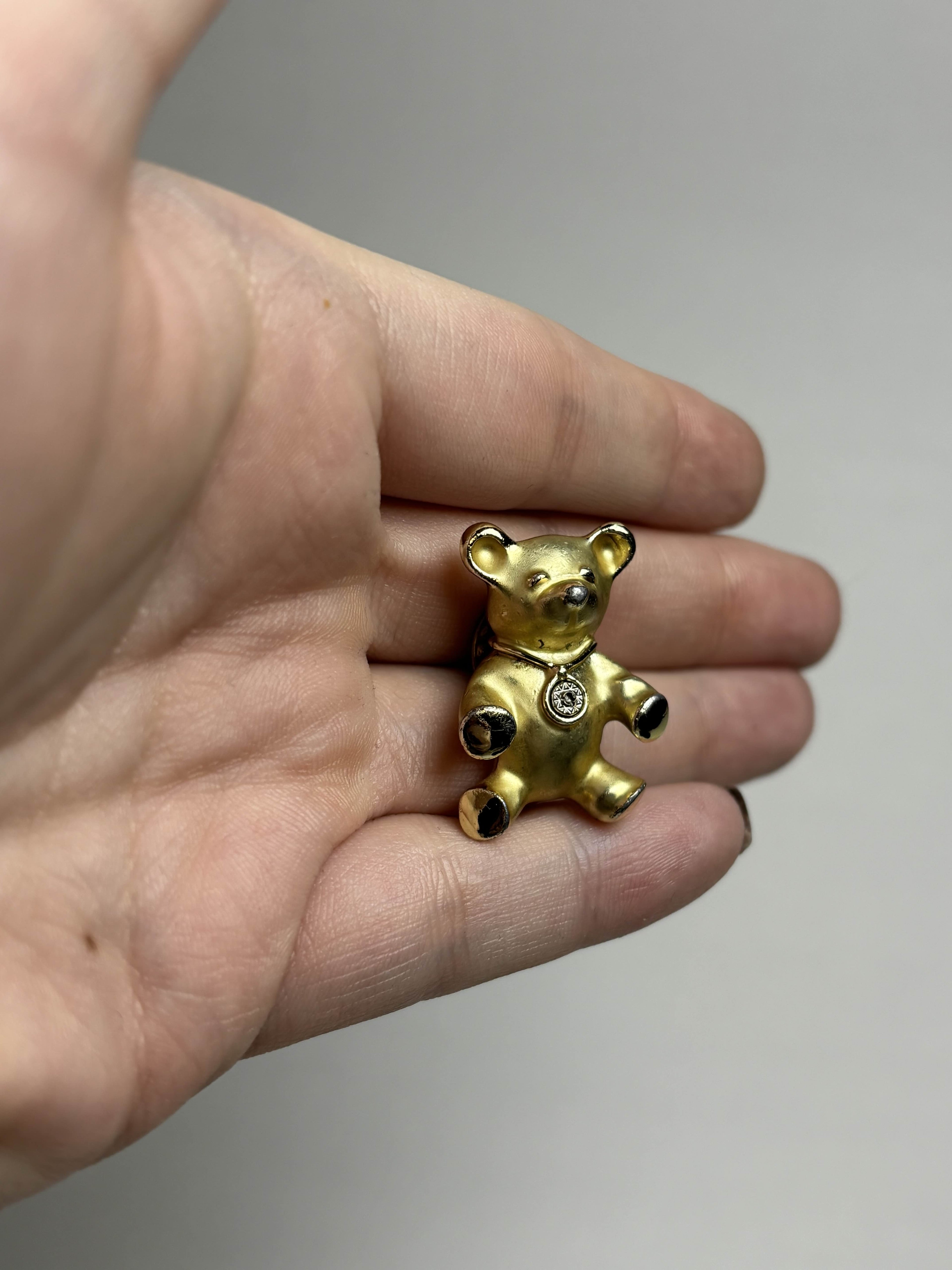 Front of old teddy bear pin held in a hand against a neutral background