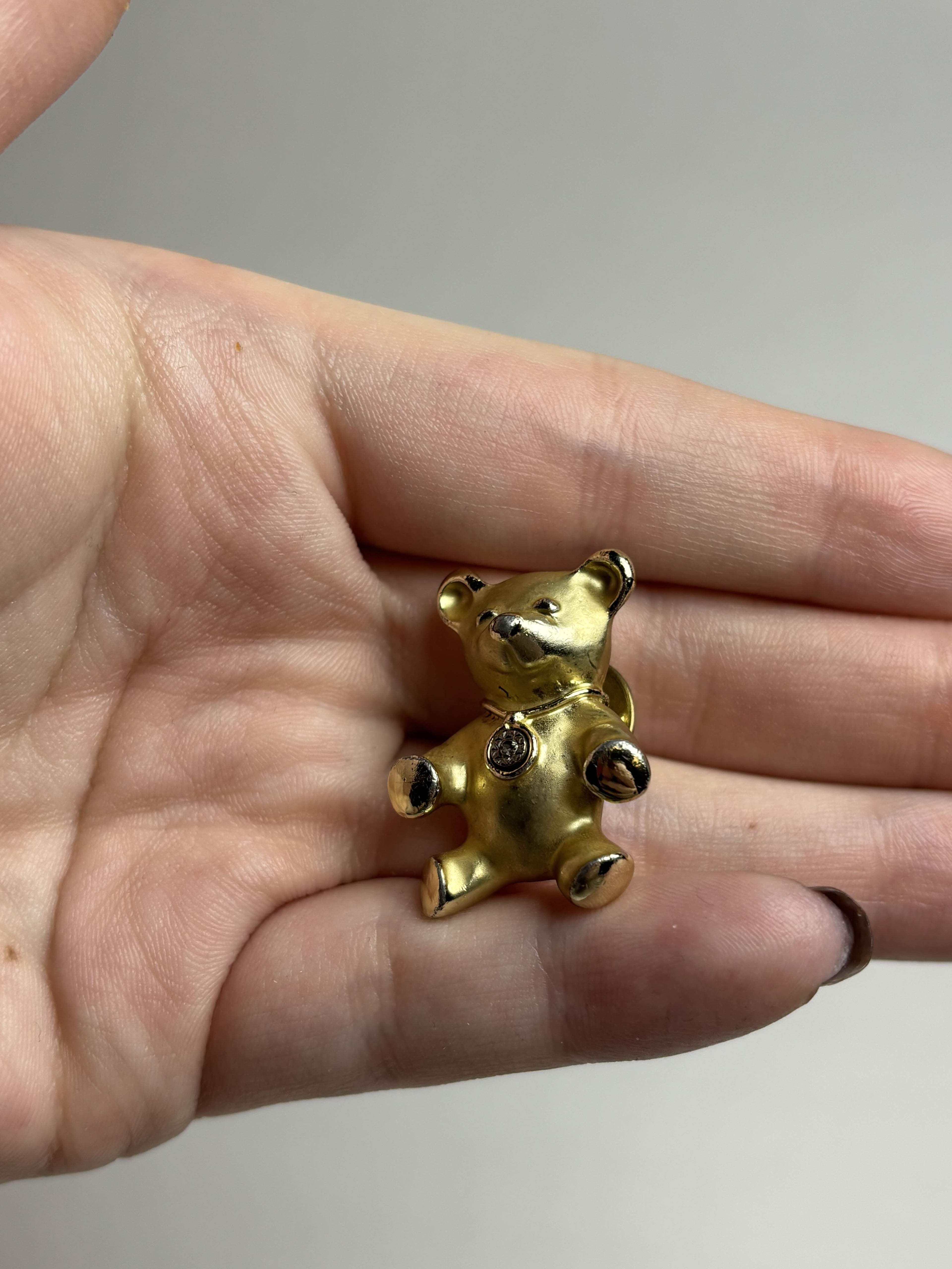 Front of old teddy bear pin held in a hand against a neutral background
