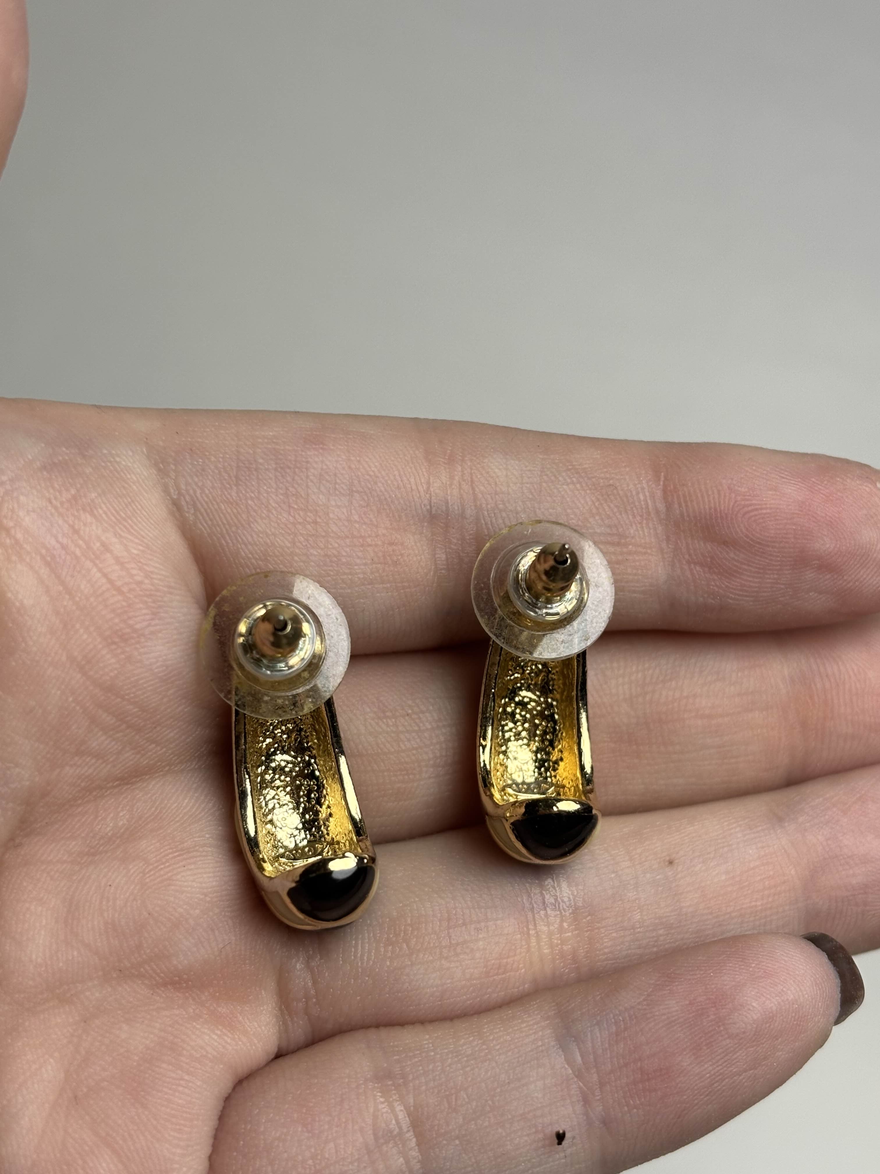 Back of pair of black, cream and gold earrings held between fingers on a neutral background