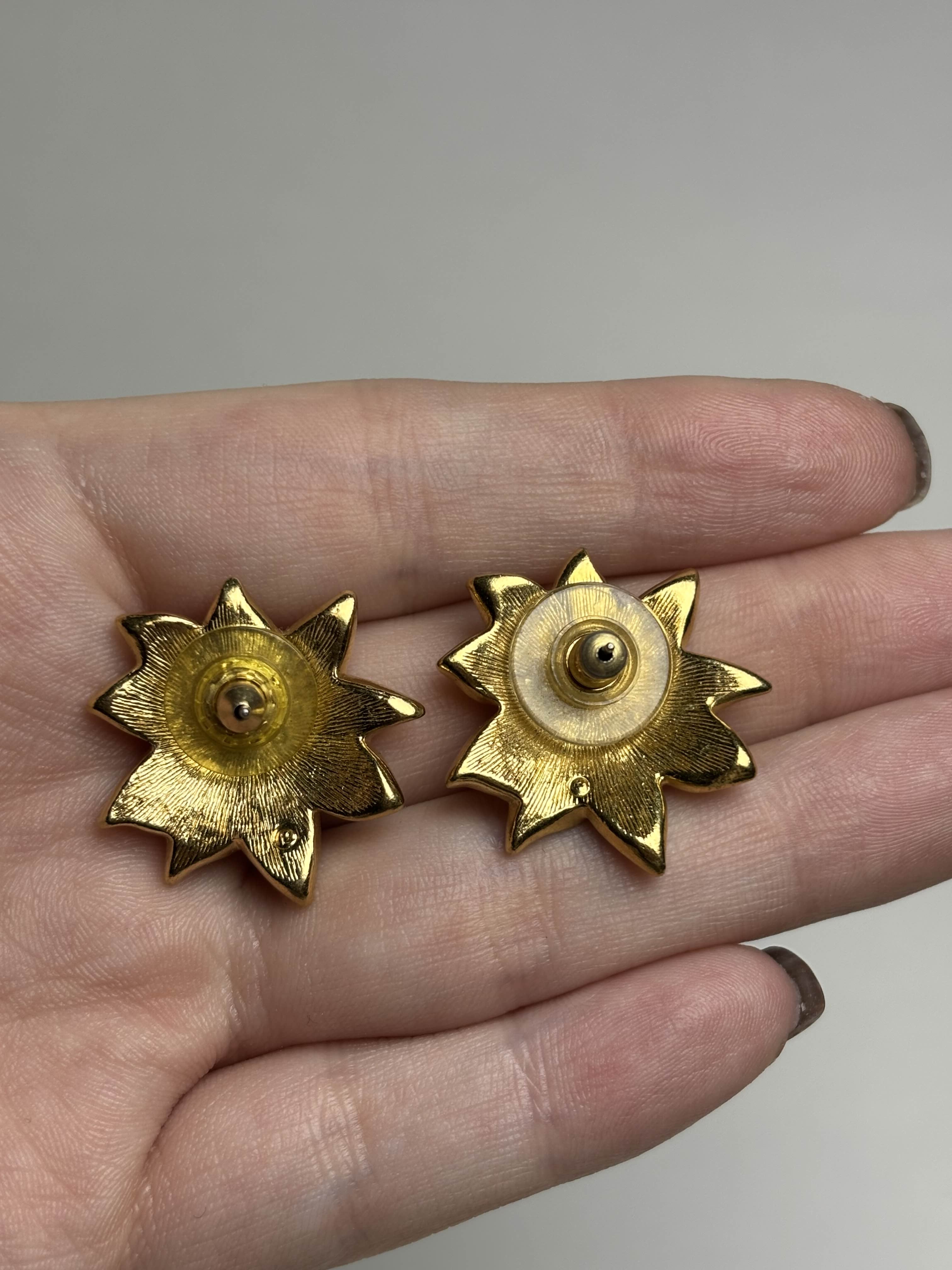 Back of Poinsettia shaped earrings held in a hand against a neutral background