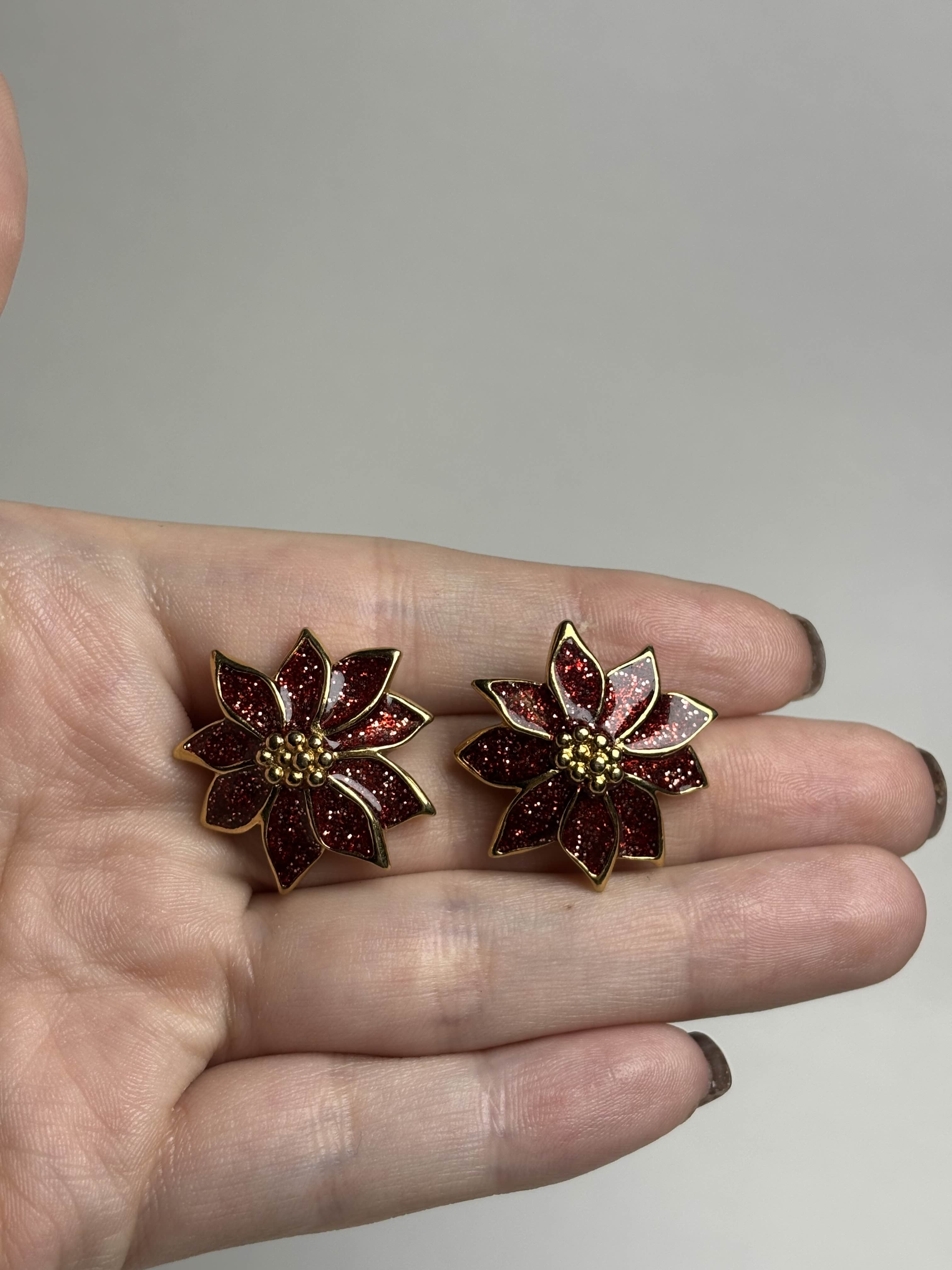 Front of red Poinsettia shaped earrings held in a hand against a neutral background