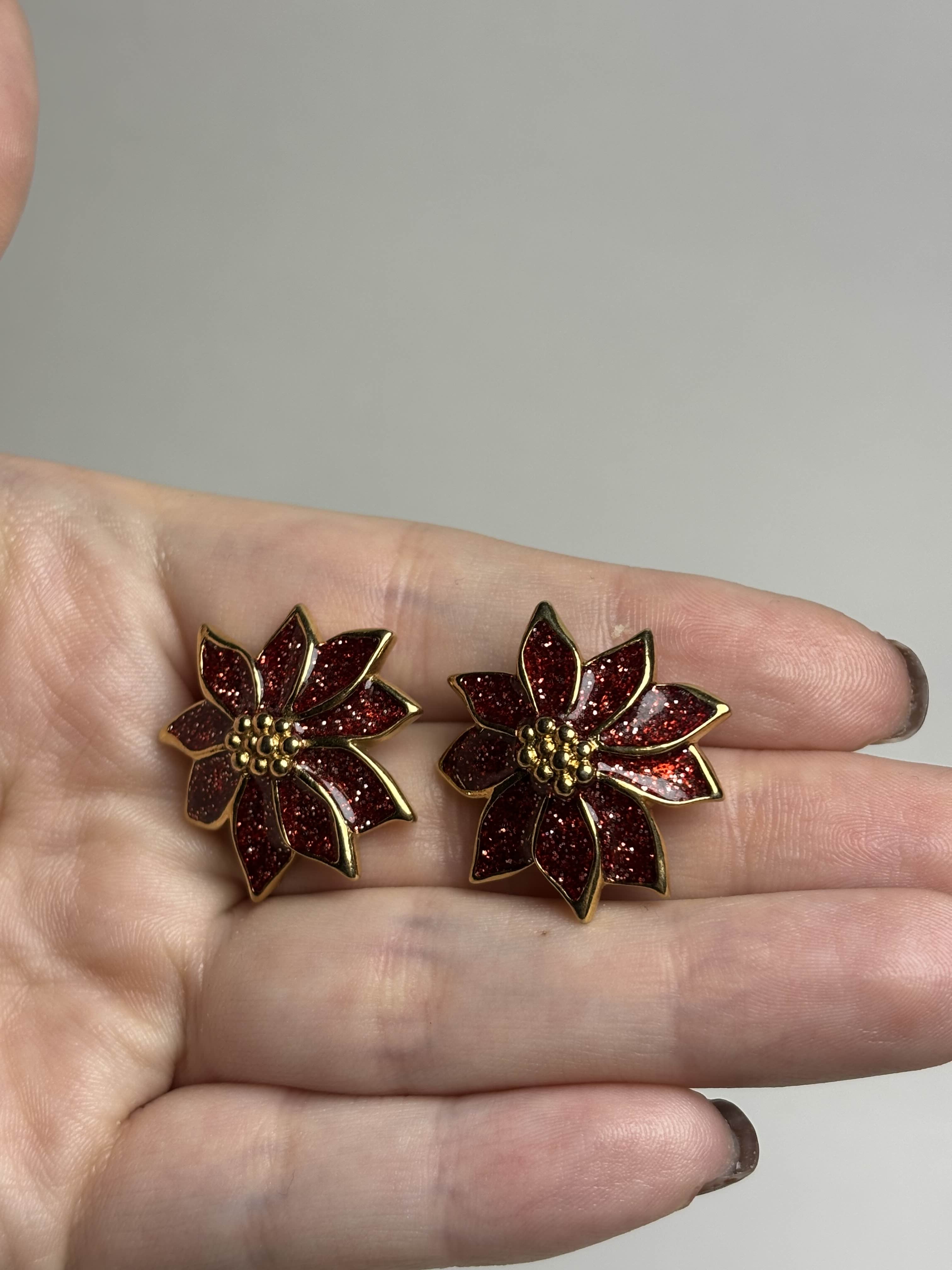 Front of red Poinsettia shaped earrings held in a hand against a neutral background
