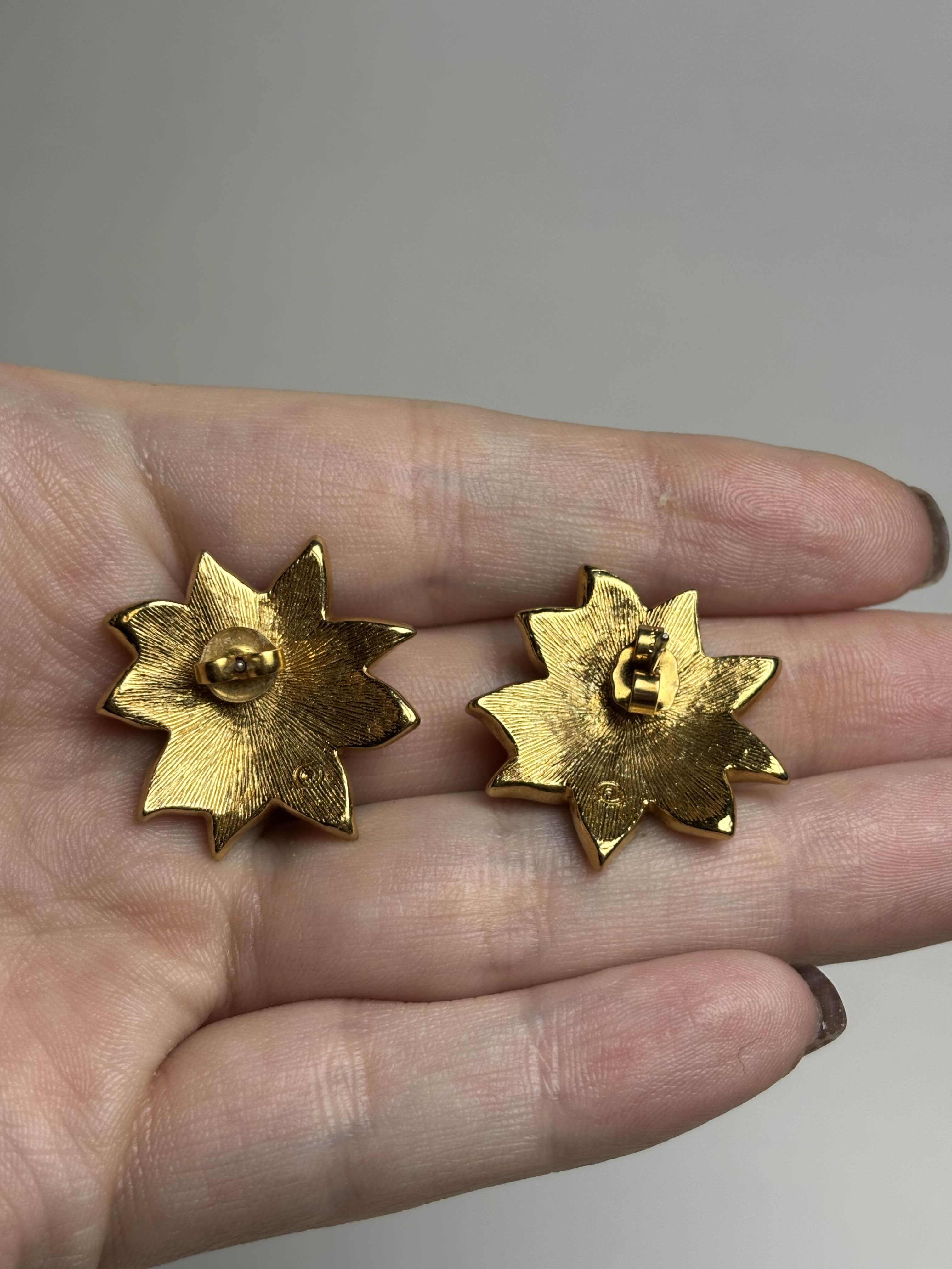 Back of red Poinsettia shaped earrings held in a hand against a neutral background