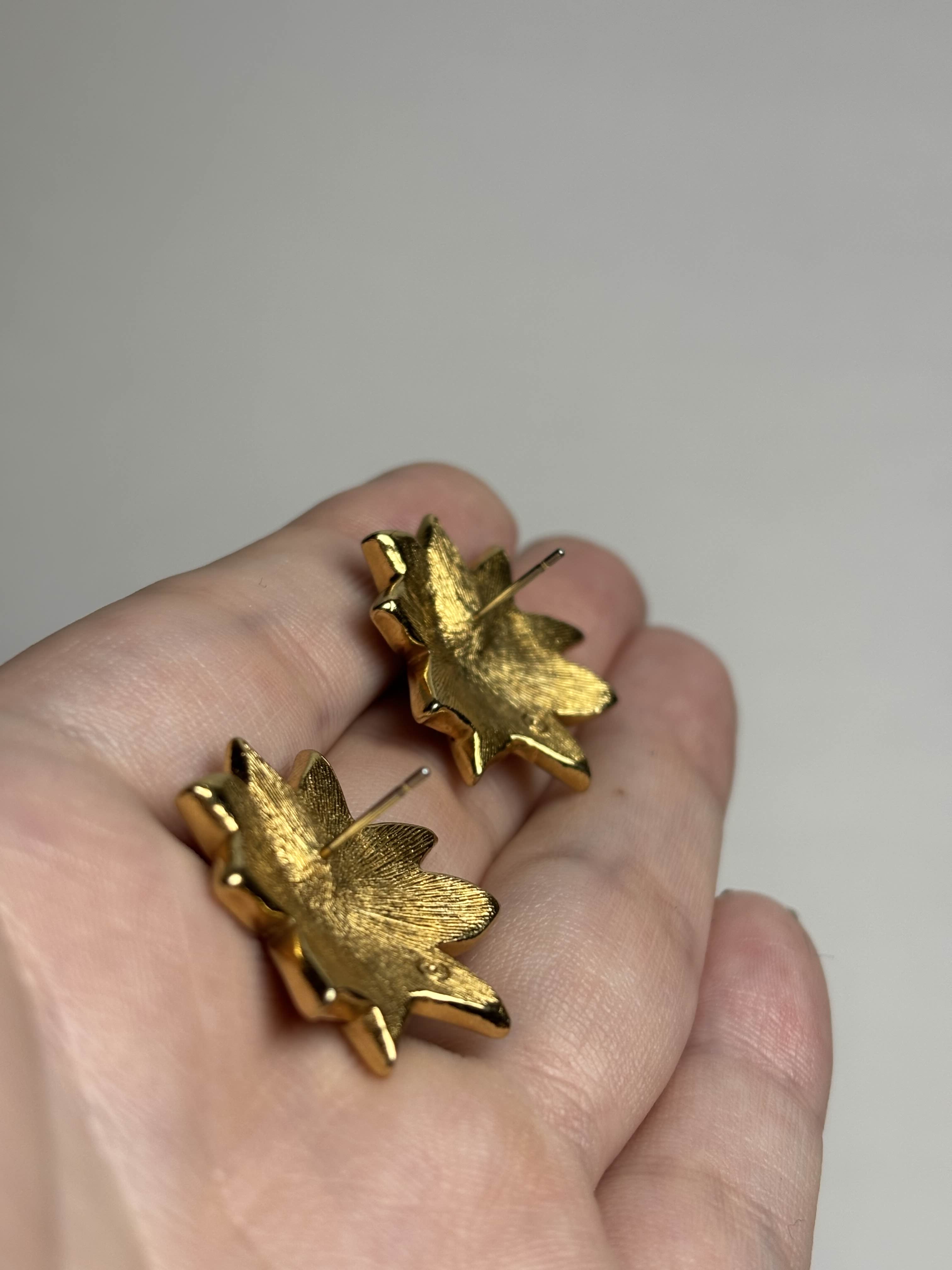 Front of red Poinsettia shaped earrings showing posts held in a hand against a neutral background