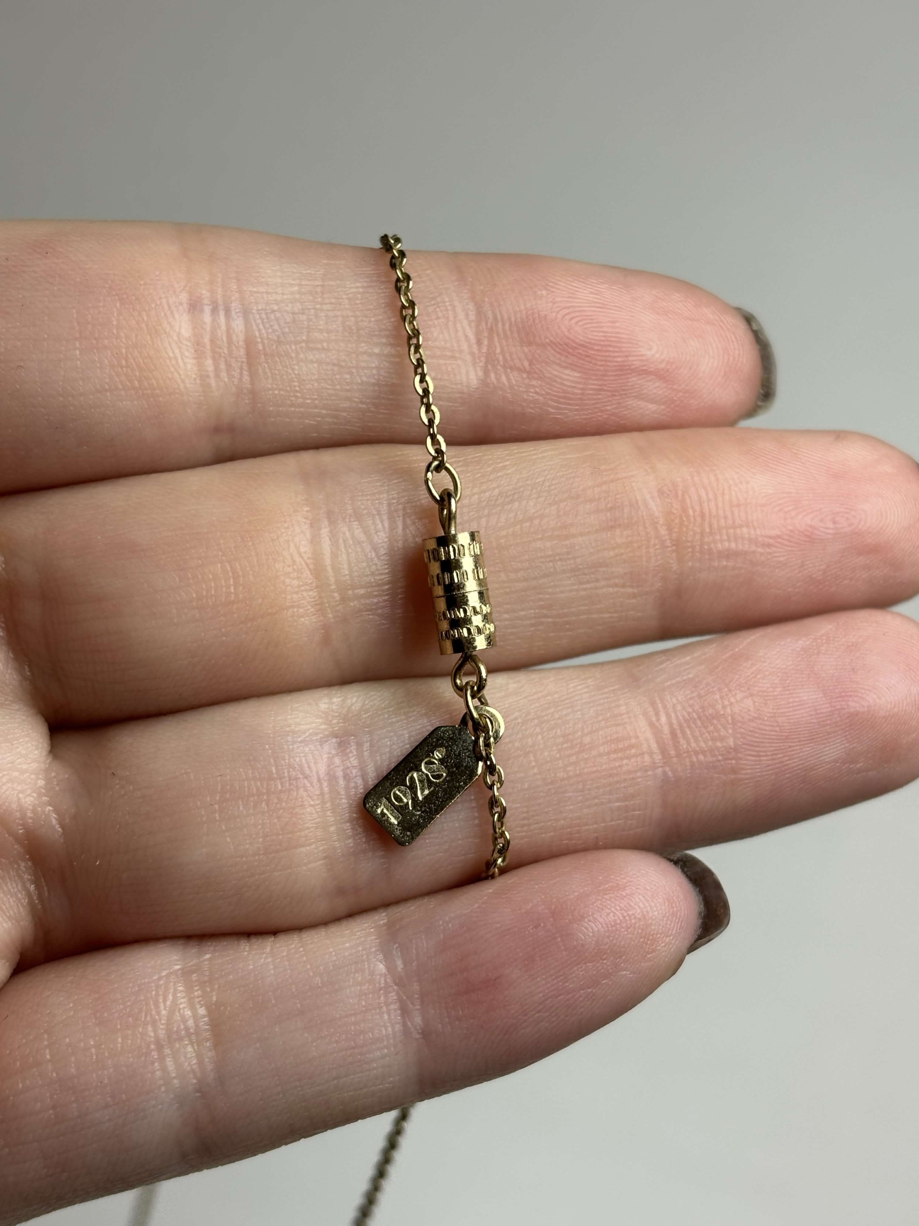Back of gold necklace held in a hand against a neutral background