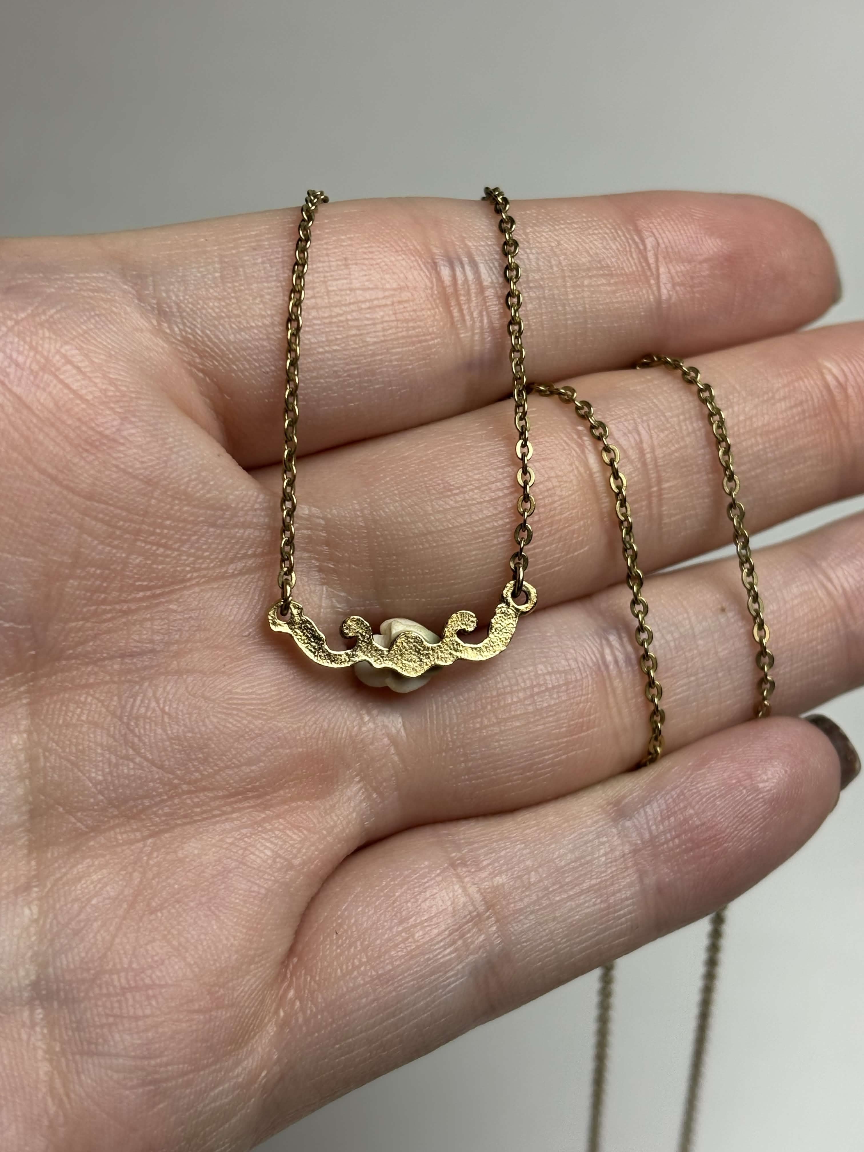 Back of pendant of gold tone necklace held in hand with neutral background