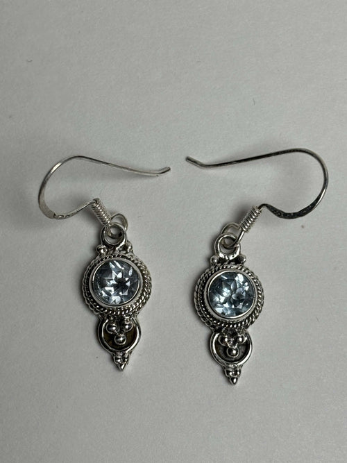 Front of silver dangle earrings with light blue round topaz on a neutral background