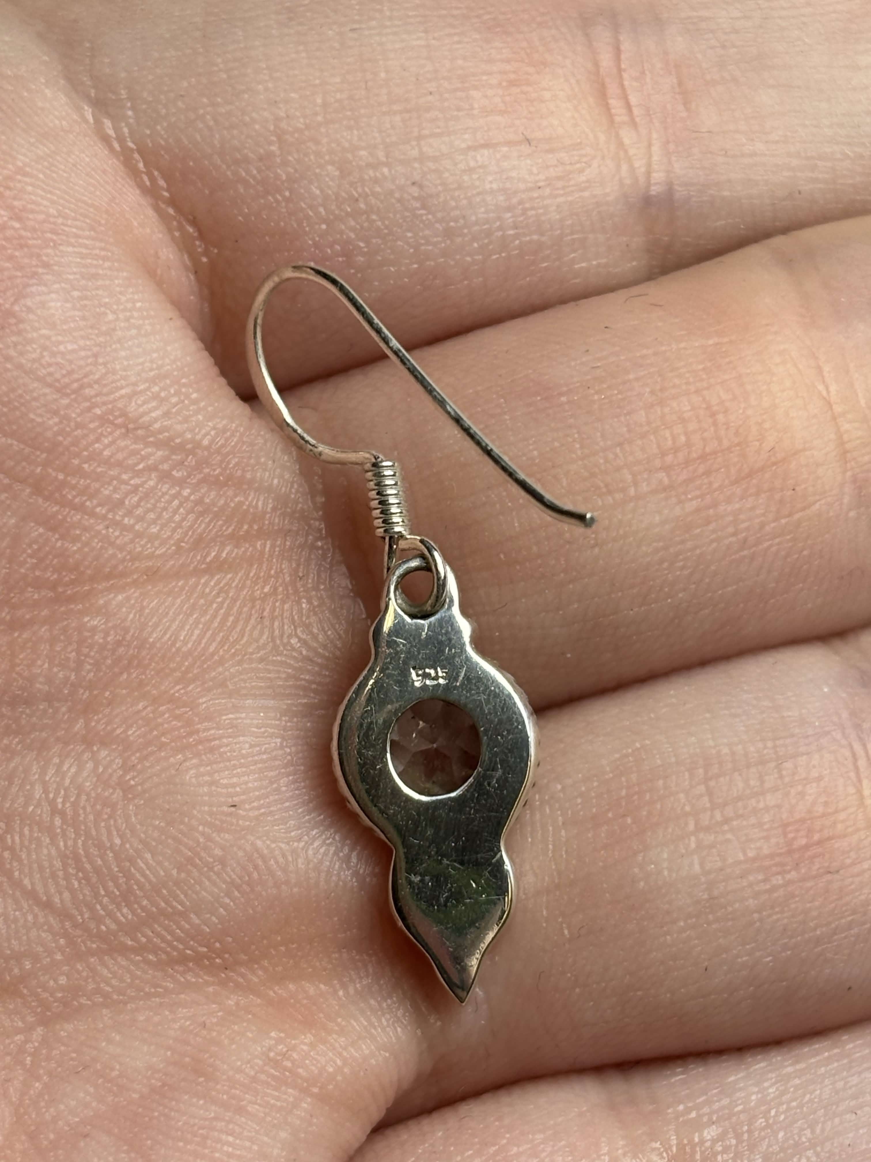 Back of silver dangle earrings showing stamp on a hand with a neutral background