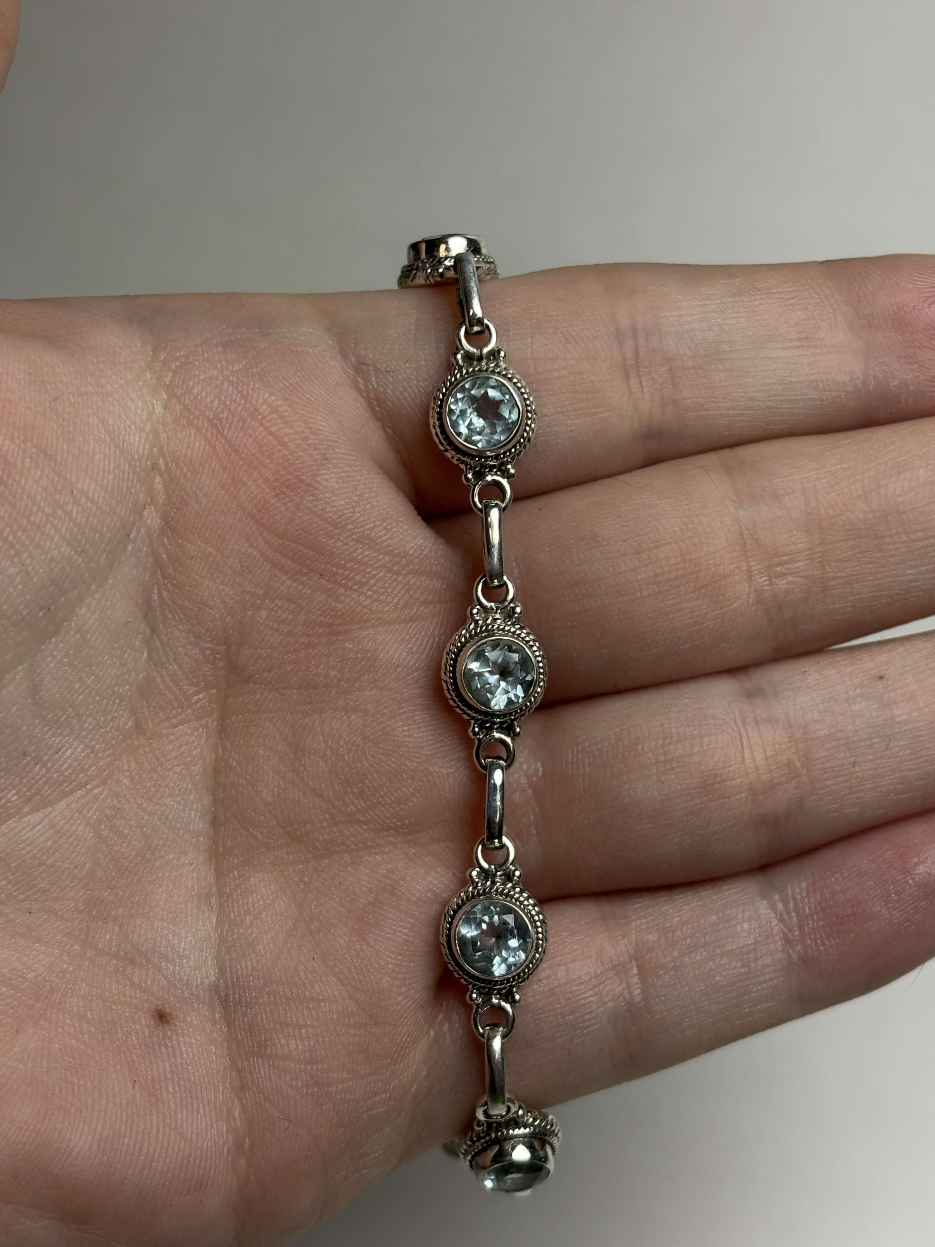Front of silver bracelet with round light blue gemstones on a hand on a neutral background