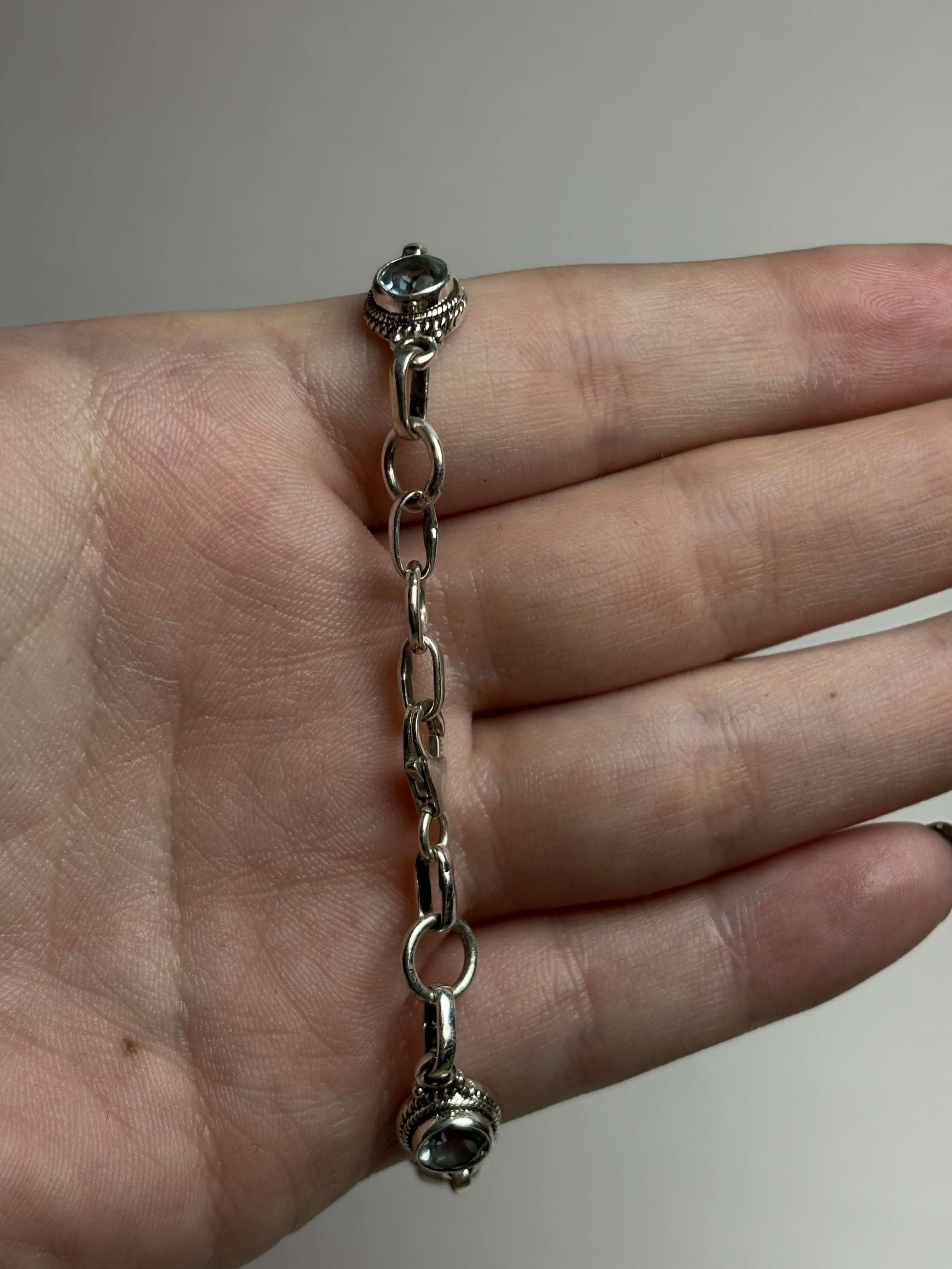 Clasp of silver bracelet with round light blue gemstones on a hand on a neutral background