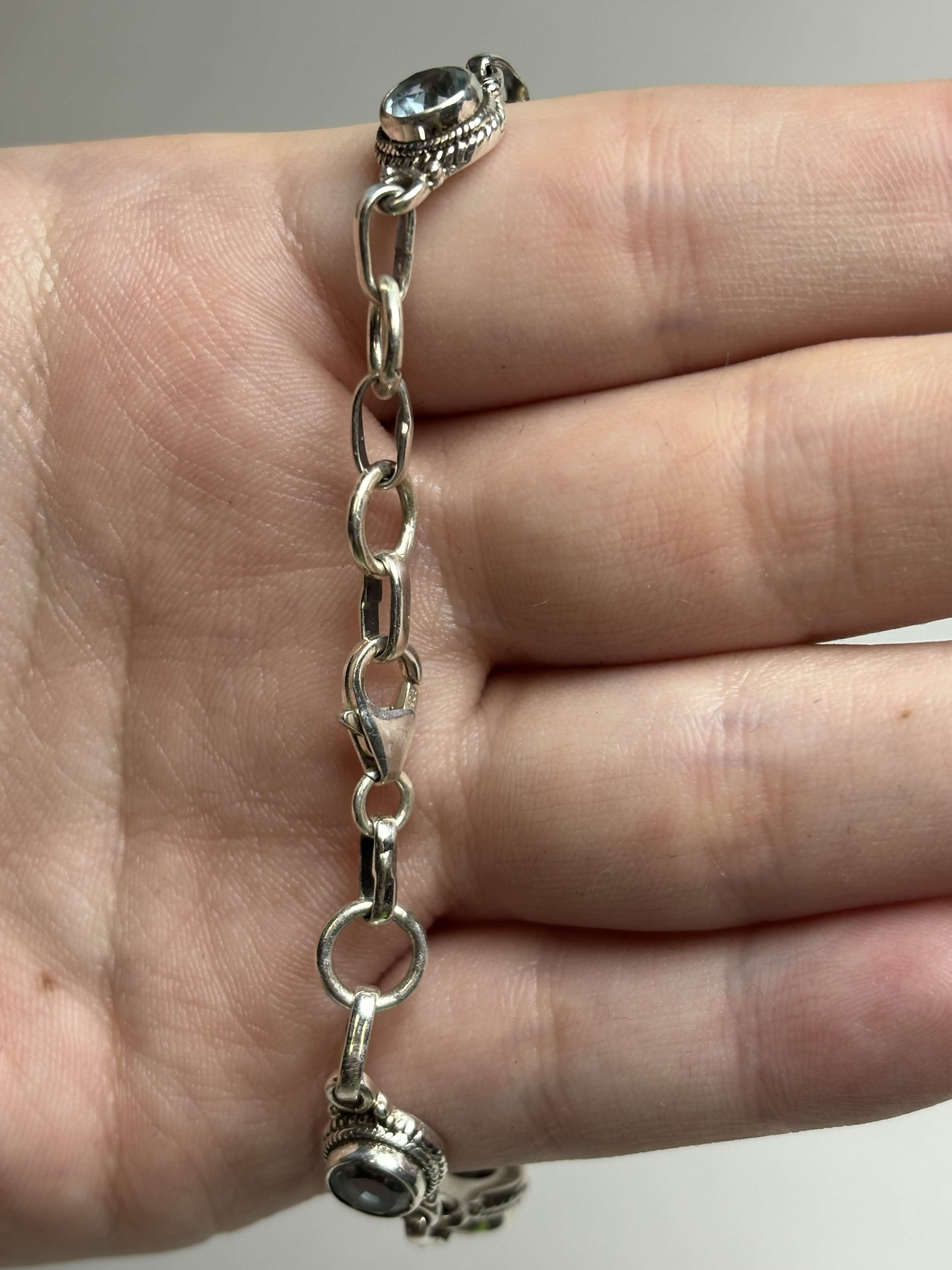 Clasp of silver bracelet with round light blue gemstones on a hand on a neutral background