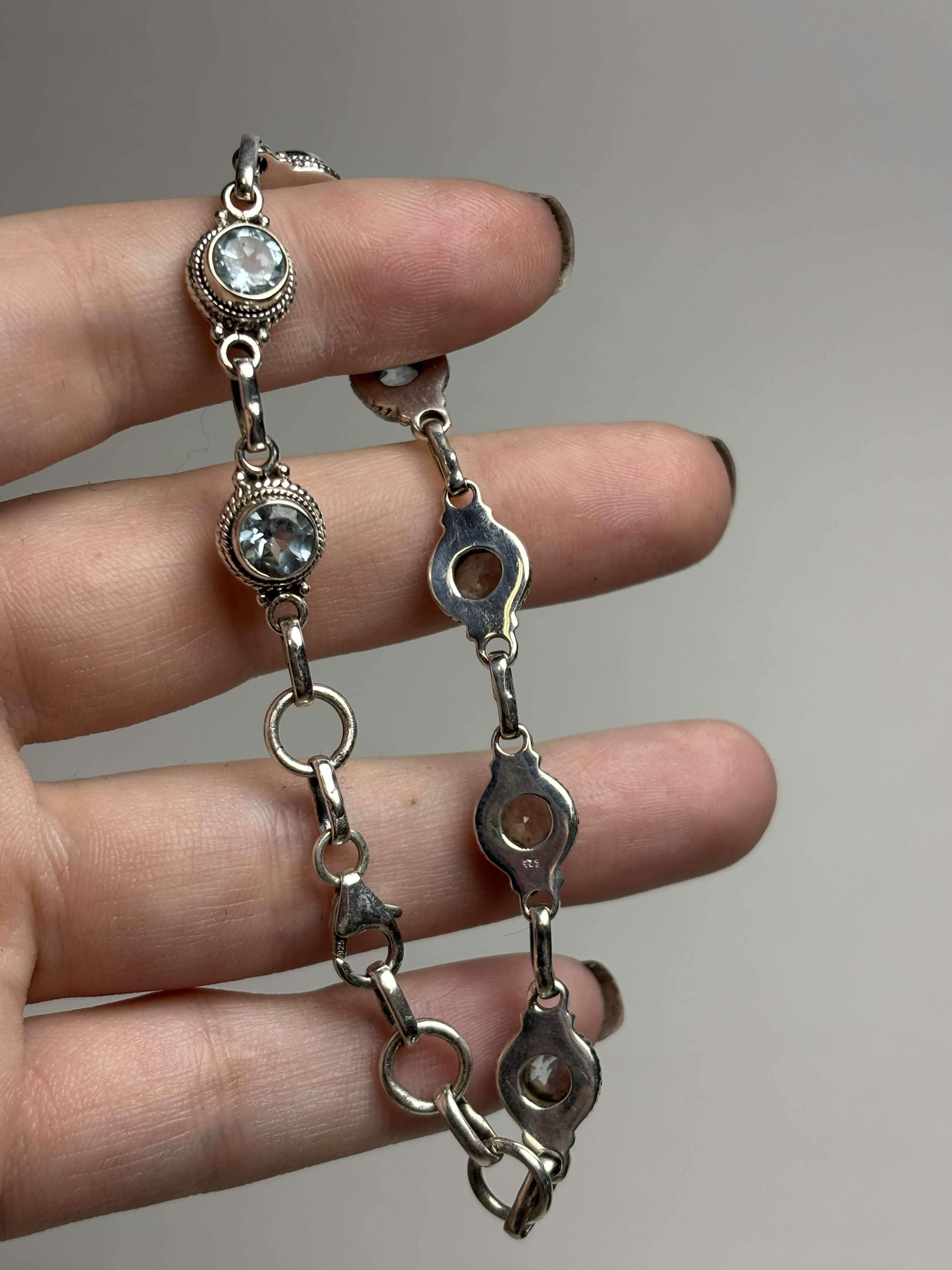 Front and back of silver bracelet with round light blue gemstones on a hand on a neutral background