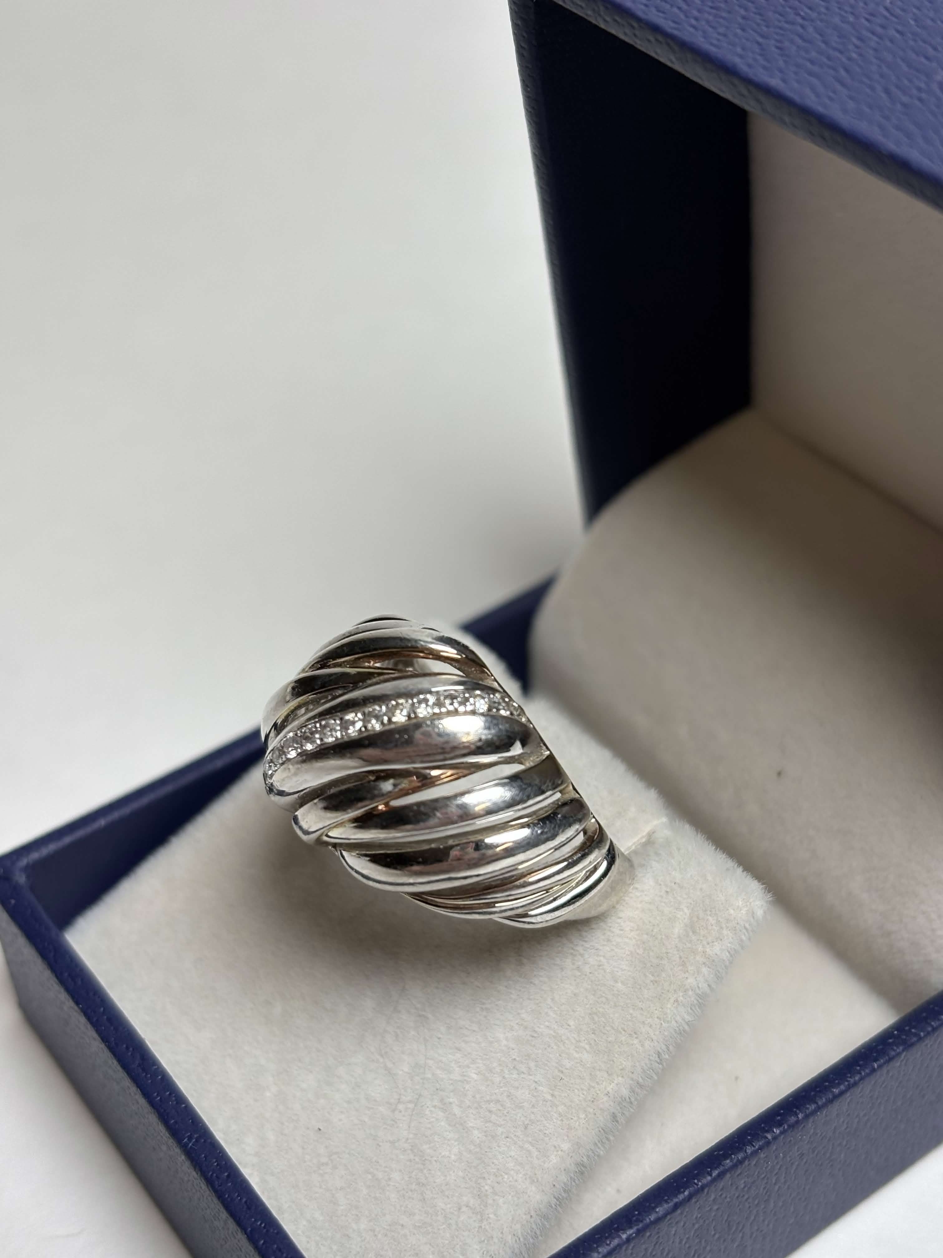 Ribbed / Shrimp / Croissant style silver ring with gold details and a band of pave diamonds in a box on a neutral background