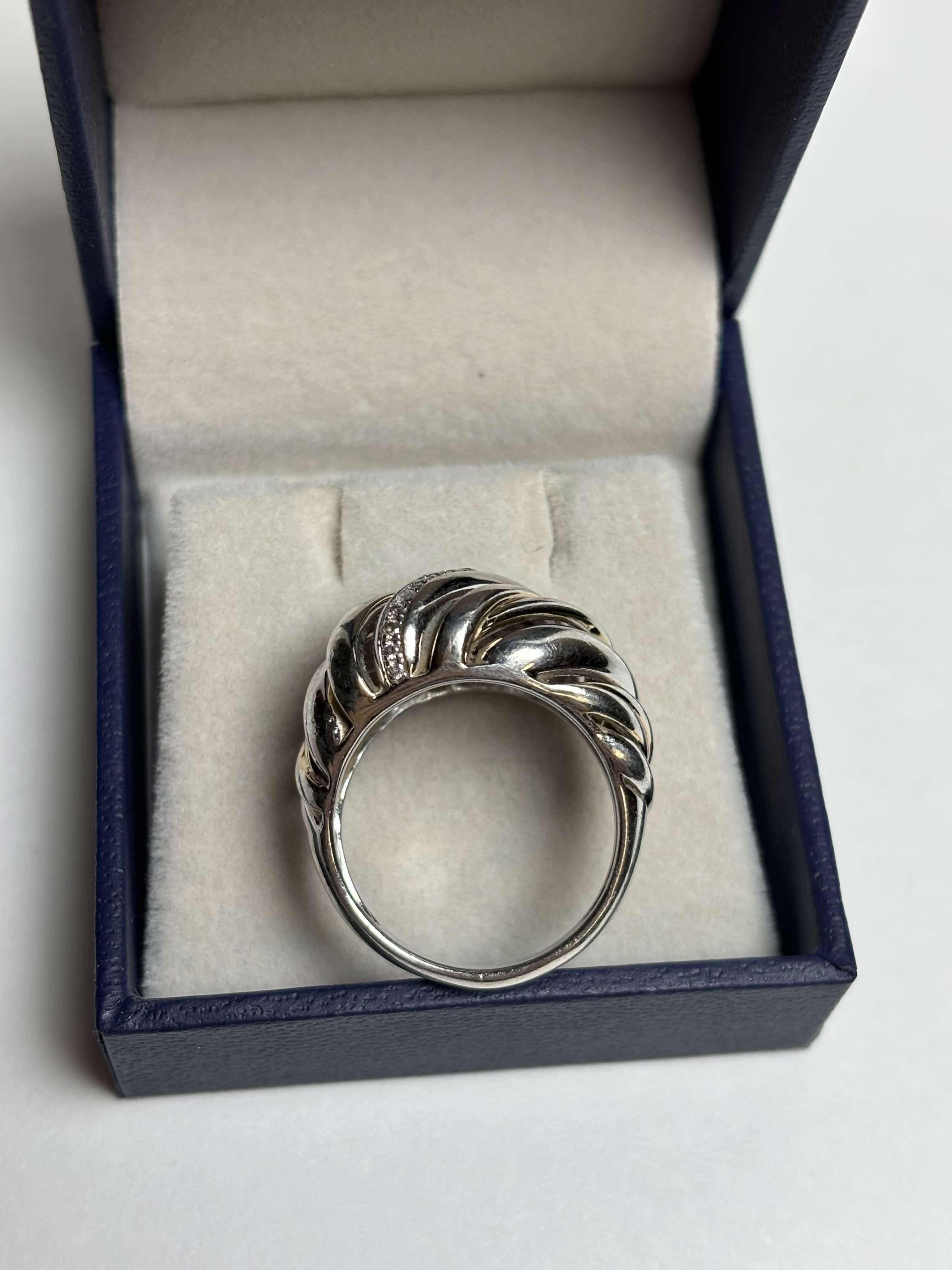 Ribbed / Shrimp / Croissant style silver ring with gold details and a band of pave diamonds in a box on a neutral background