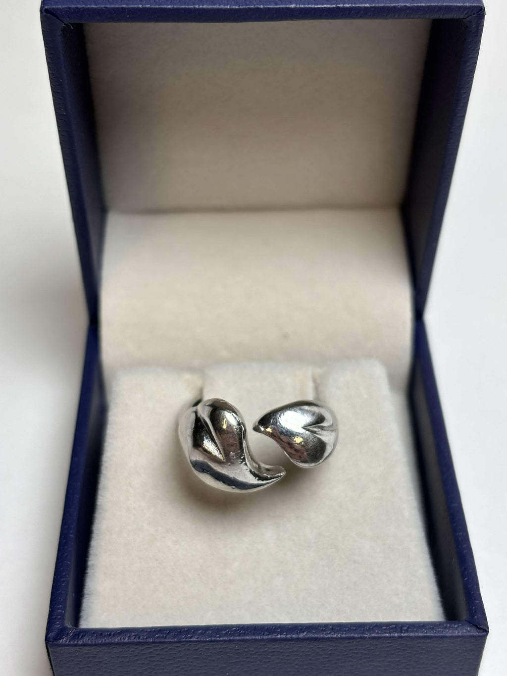 Front of silver tone ring with two heart shaped bypass in a box on a neutral background