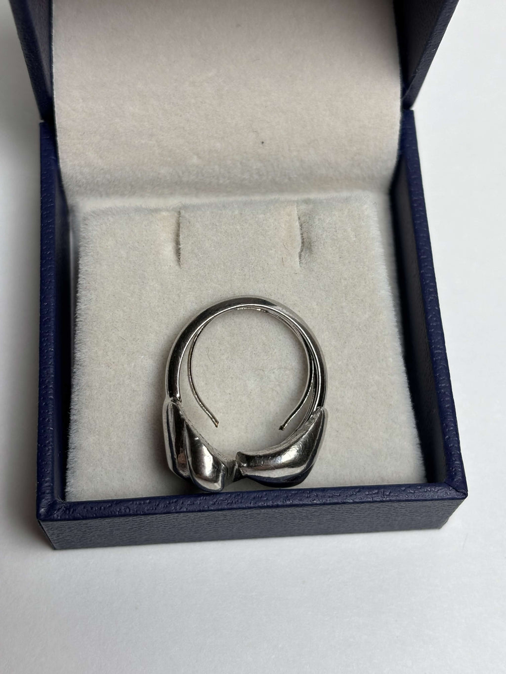 Side of silver tone ring with two heart shaped bypass in a box on a neutral background