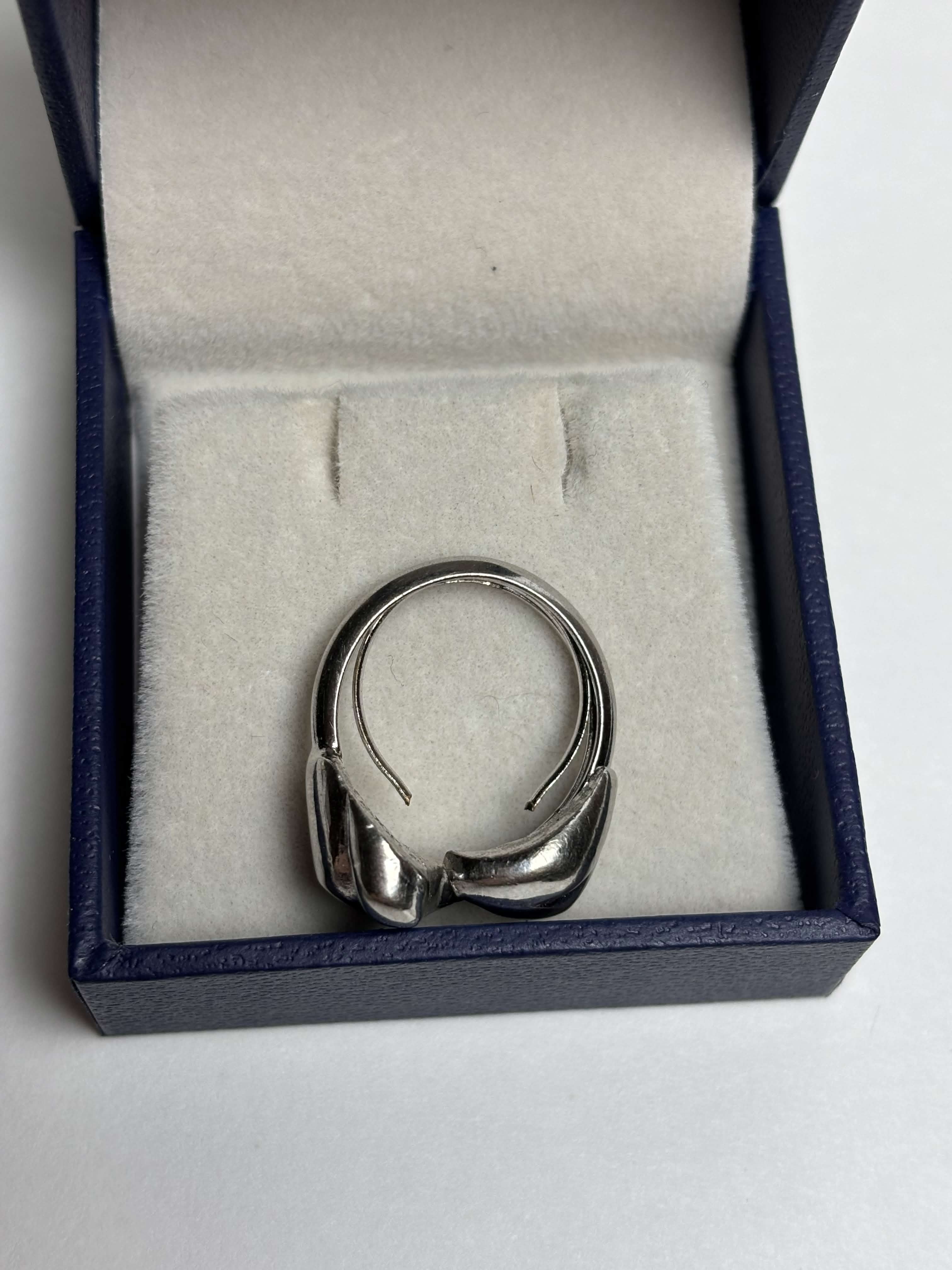 Side of silver tone ring with two heart shaped bypass in a box on a neutral background