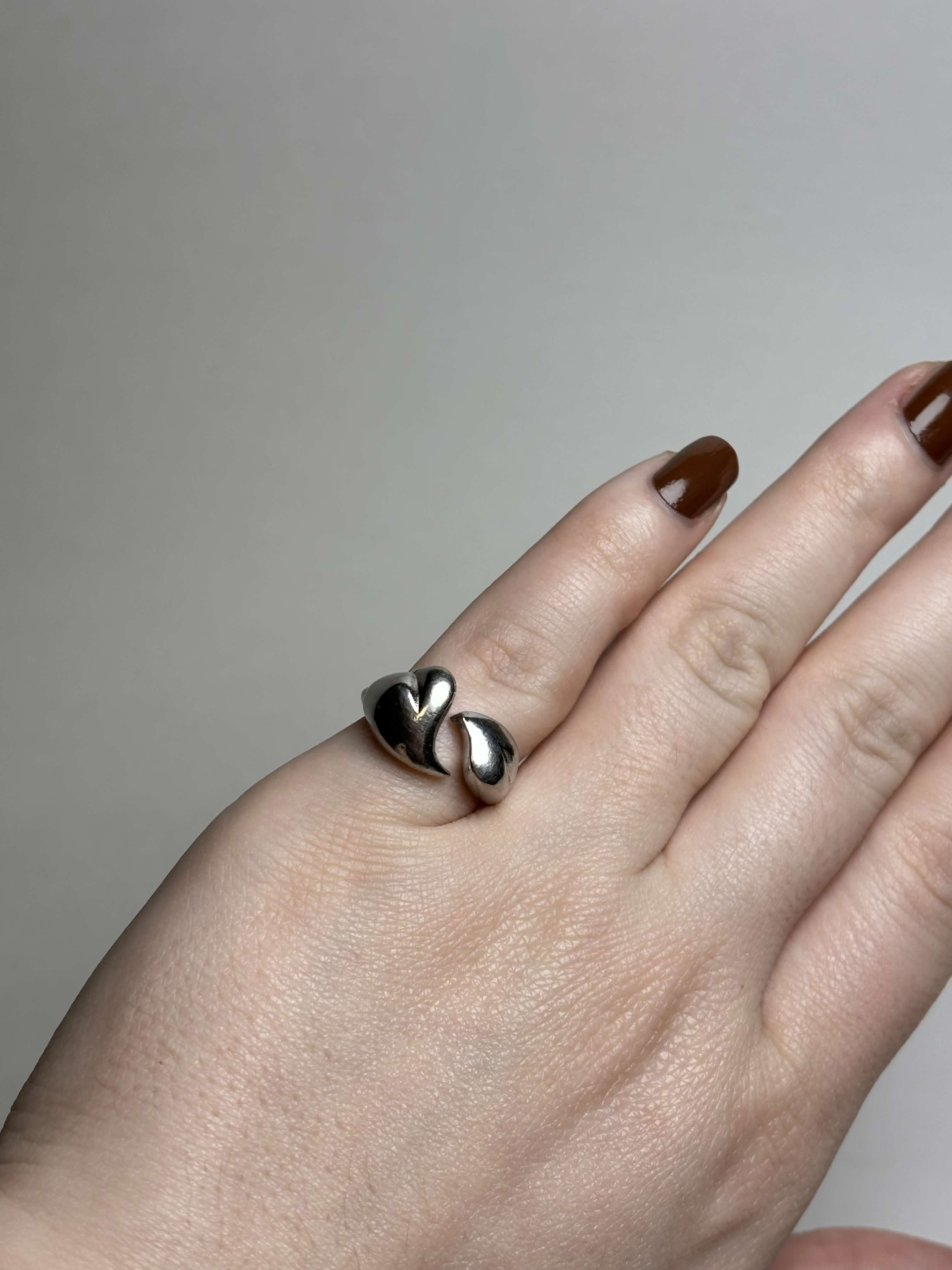 Front of silver tone ring with two heart shaped bypass on a hand on a neutral background