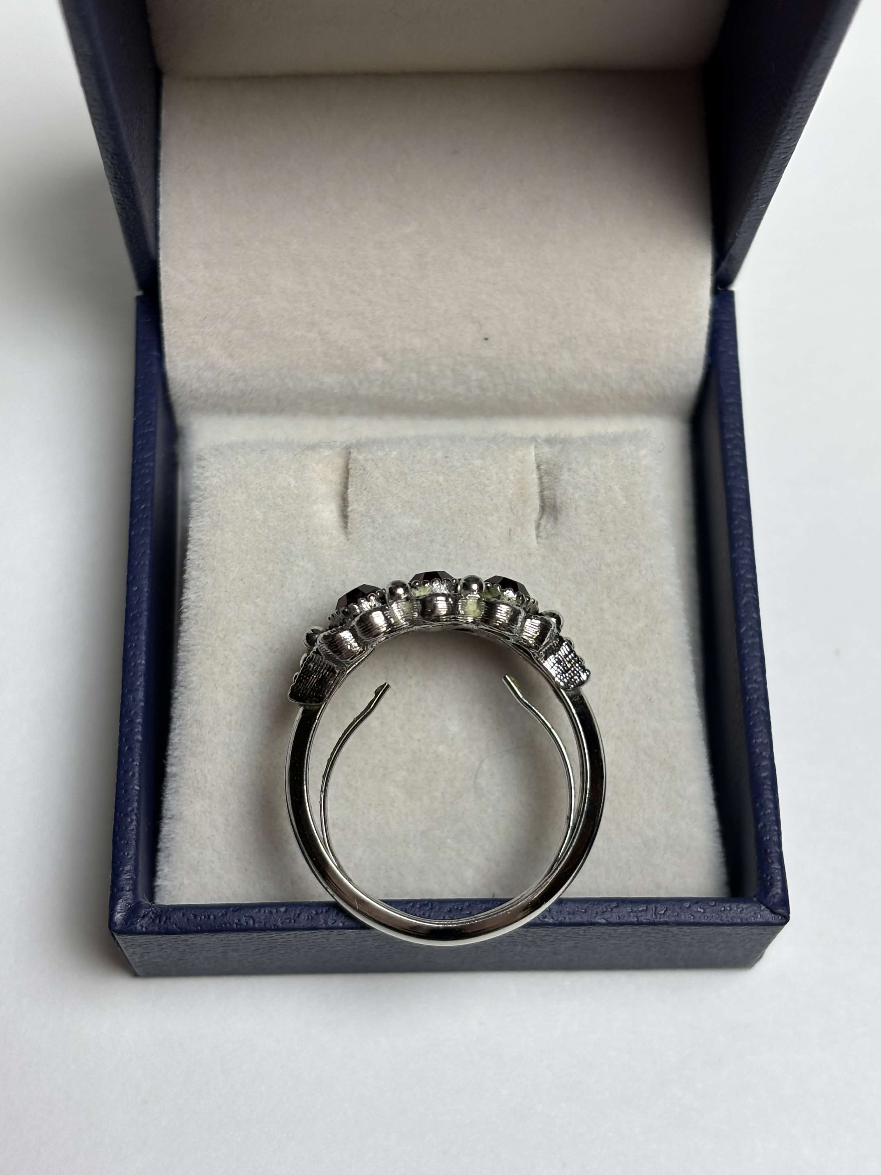 Side of silver ring with three purple stones in a box on a neutral background