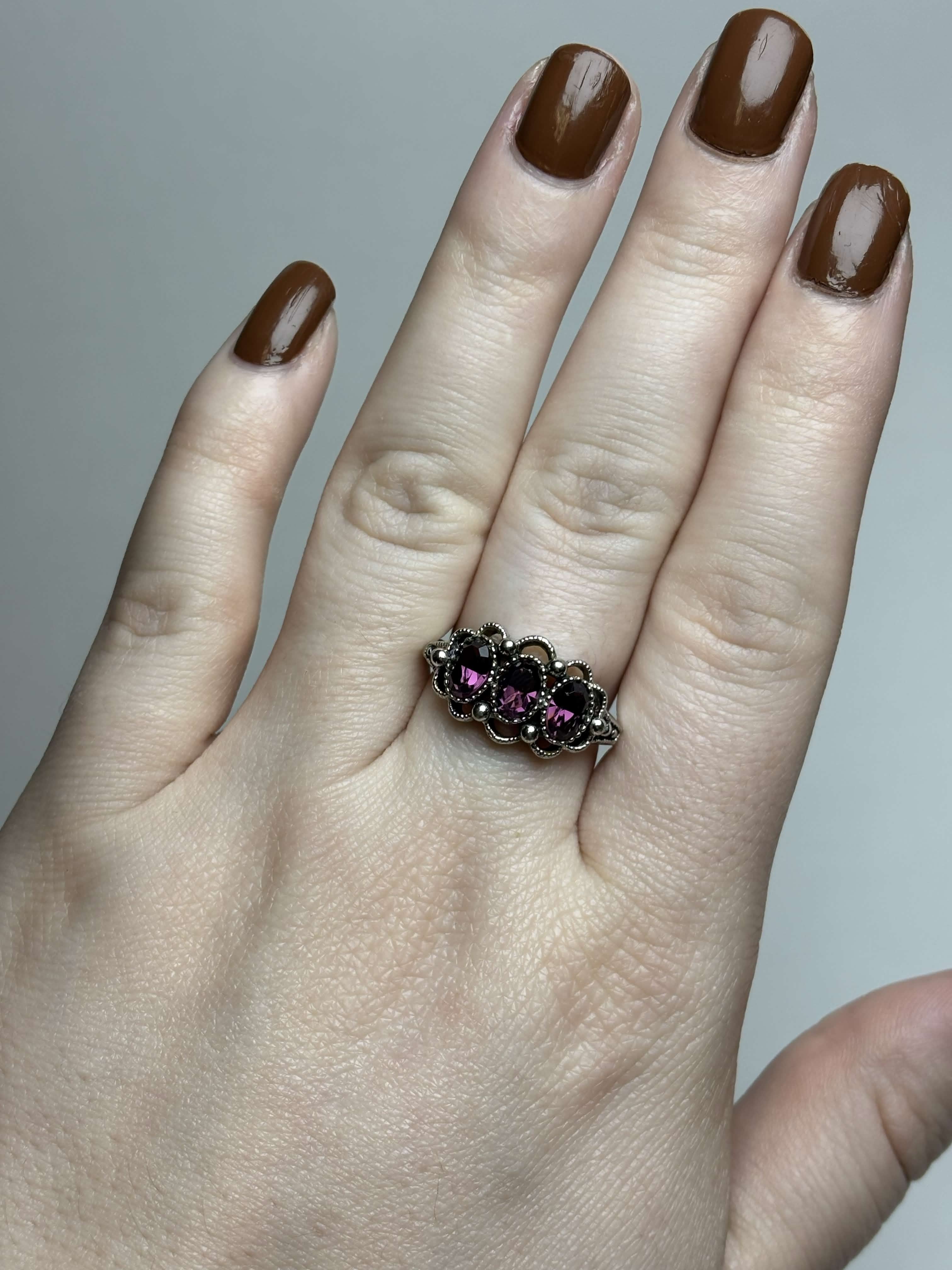 Front of silver ring with three purple stones on hand on a neutral background