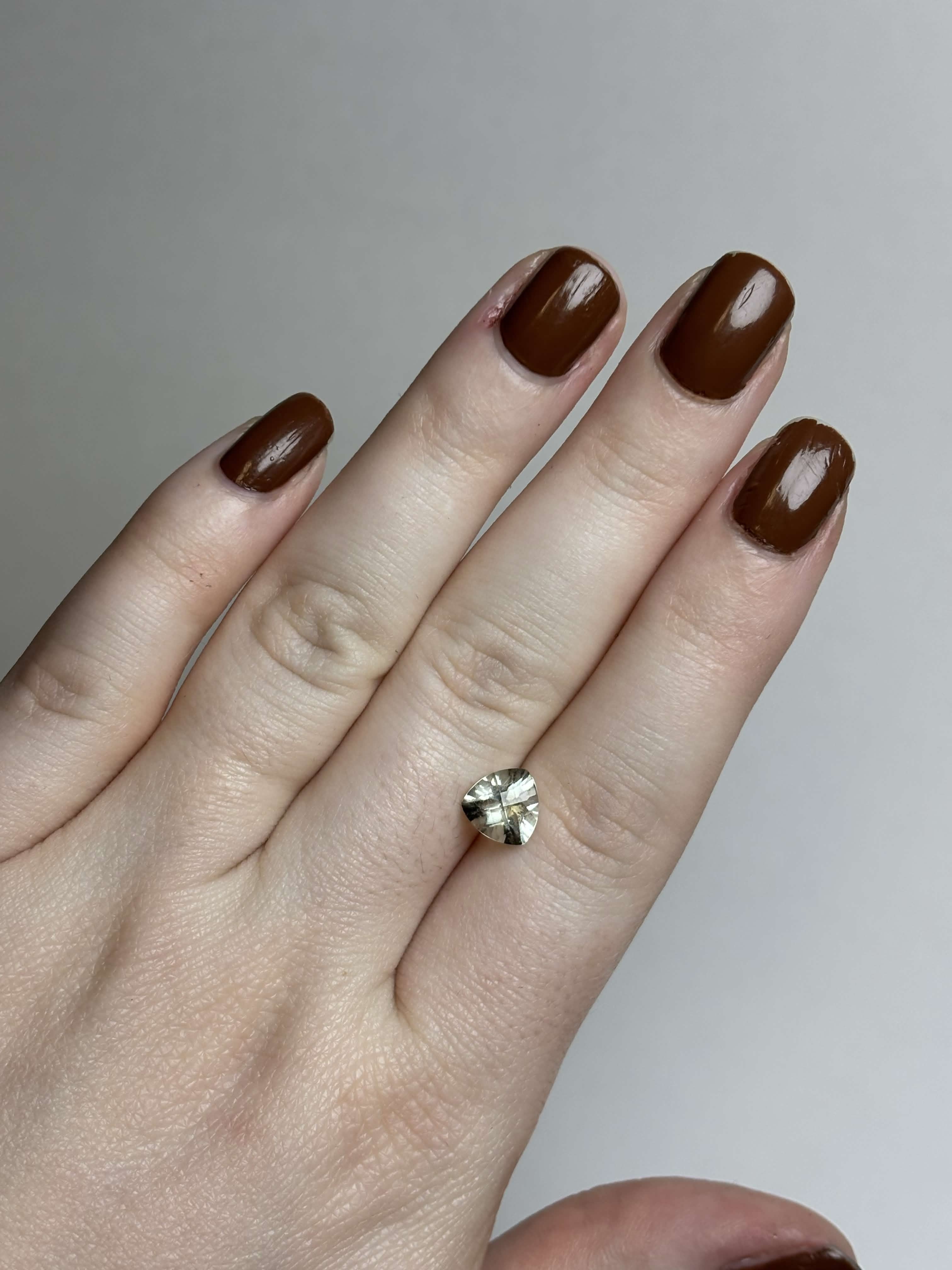 Hand with trillion cut (triangular) light green stone 8 mm in size on it