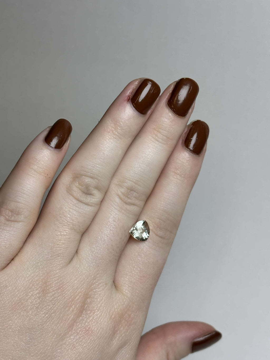 Hand with trillion cut (triangular) light green stone 8 mm in size on it