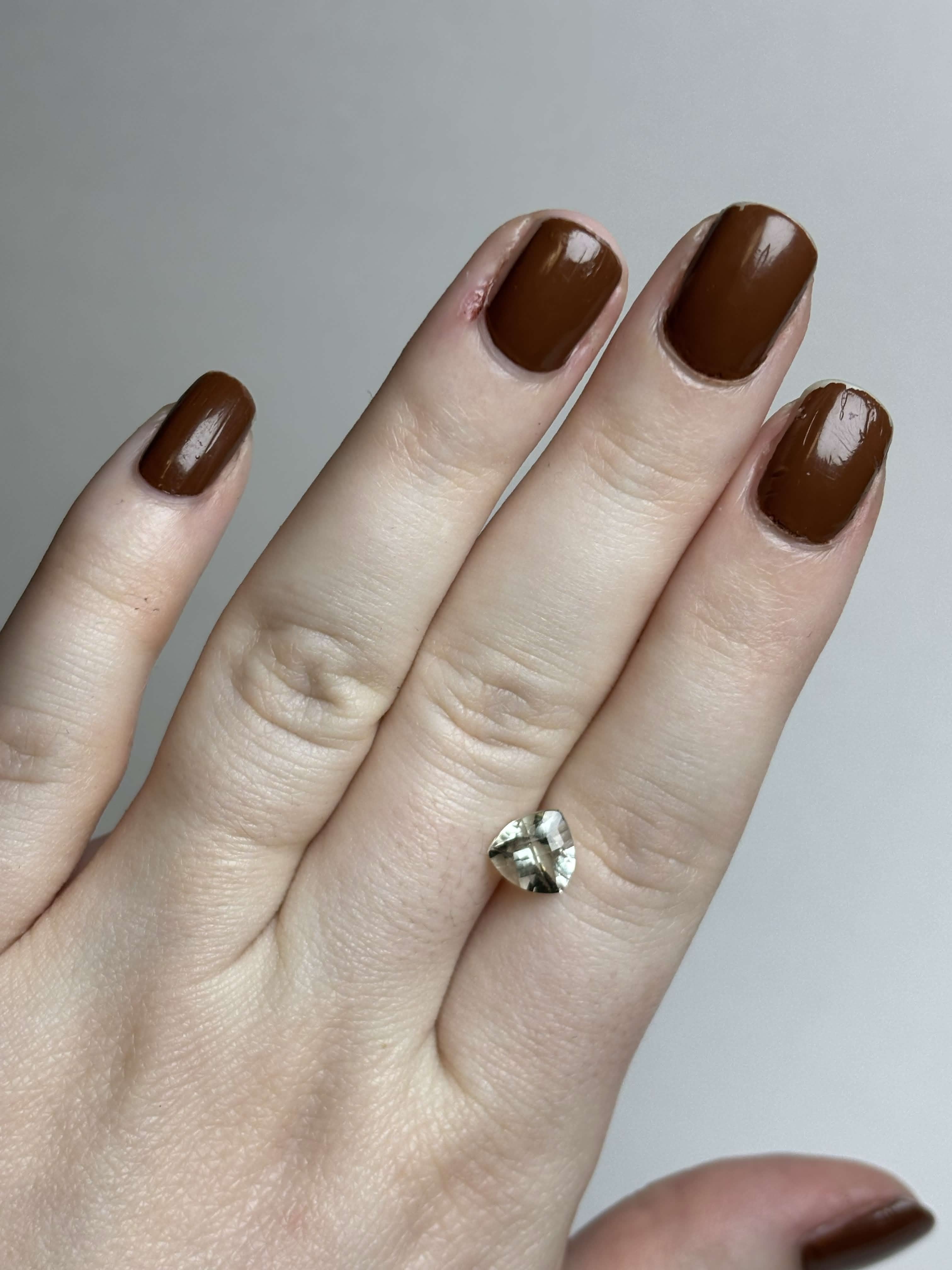 Hand with trillion cut (triangular) light green stone 8 mm in size on it